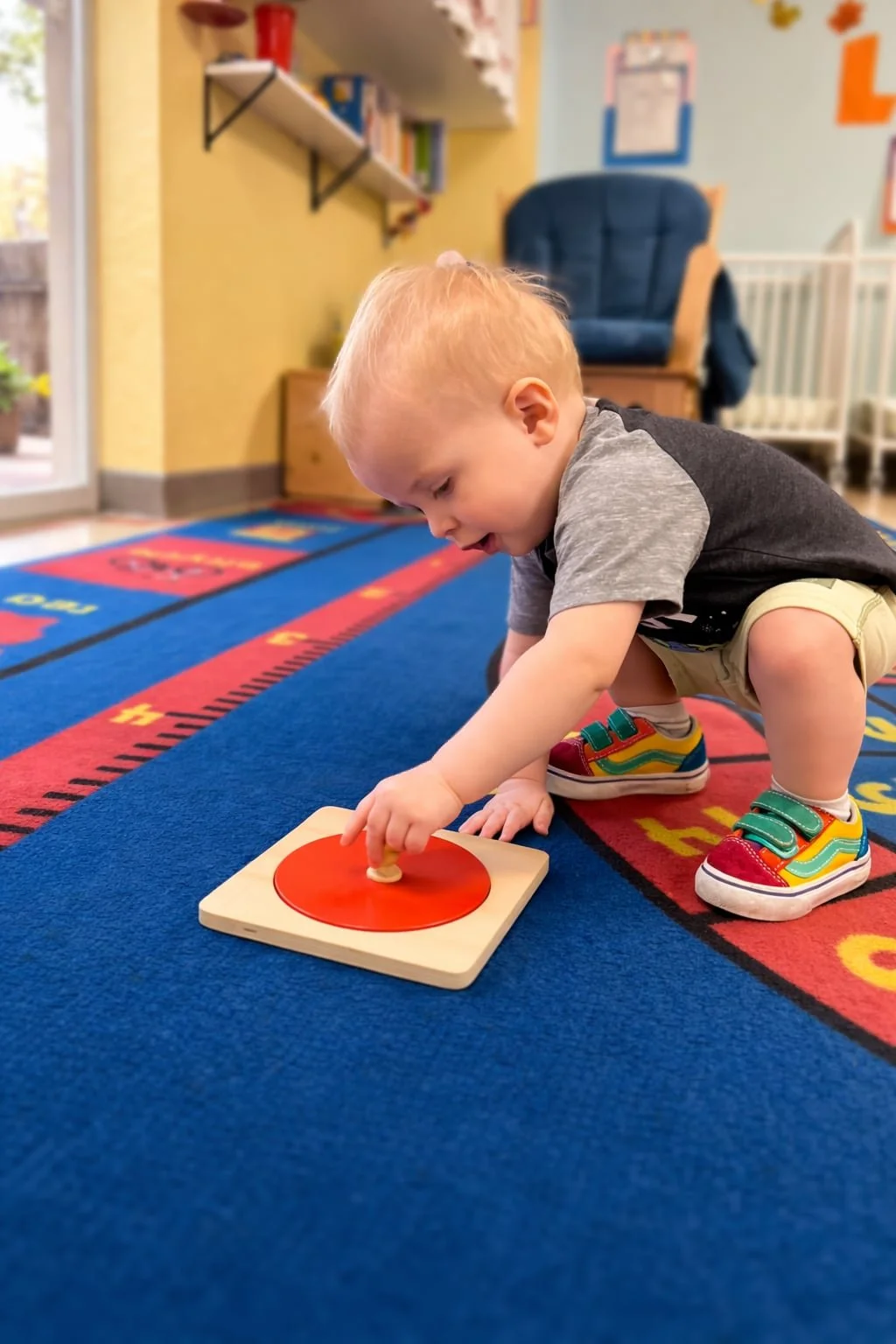 A toddler places a red circle puzzle piece into a Montessori wooden board.