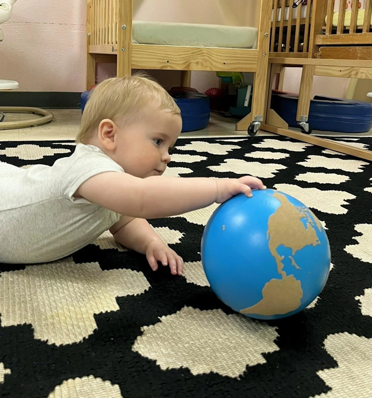 Infant exploring Montessori globe on classroom rug in Austin Montessori infant program
