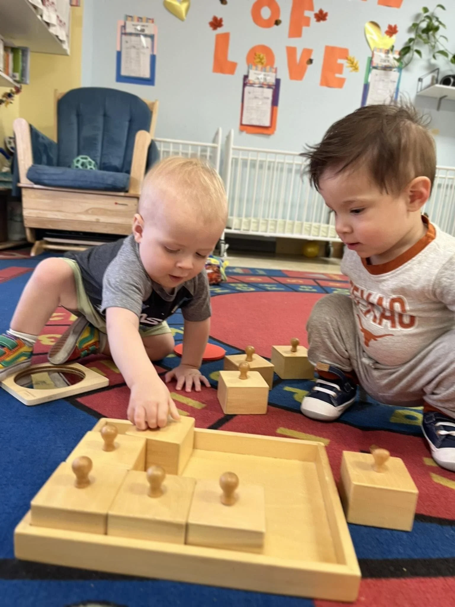 Two infants enjoy Montessori activity, fitting wooden puzzle pieces into a board in a classroom in Austin, Texas
