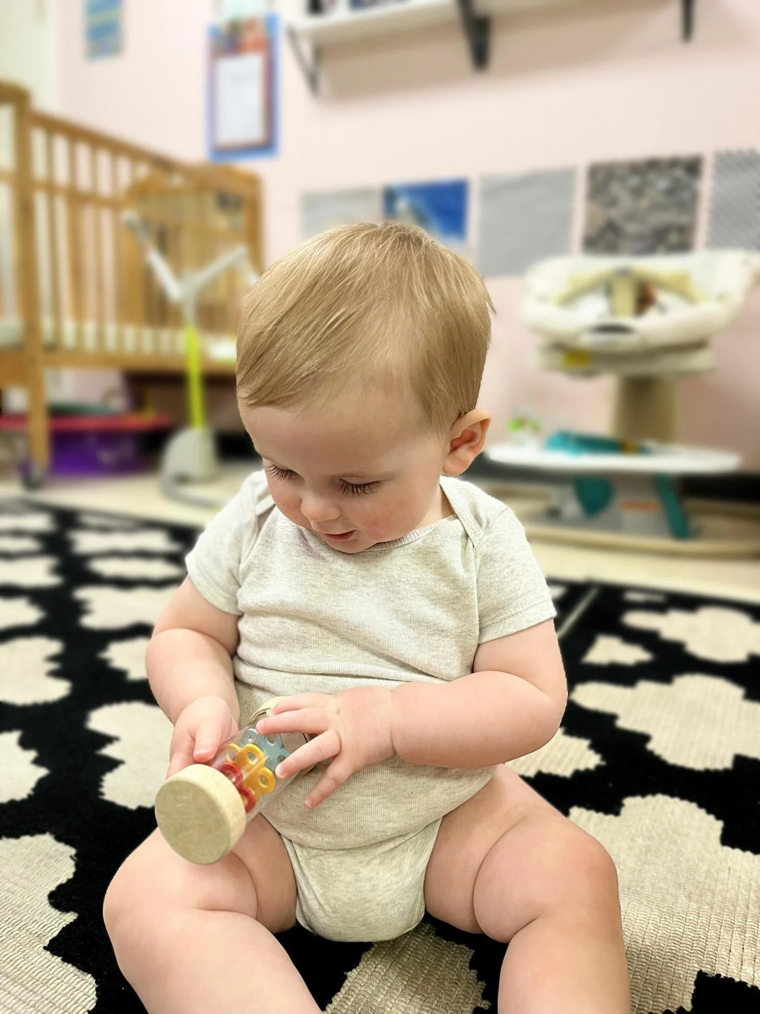 Infant sitting on a patterned rug, exploring a soft Montessori rattle.