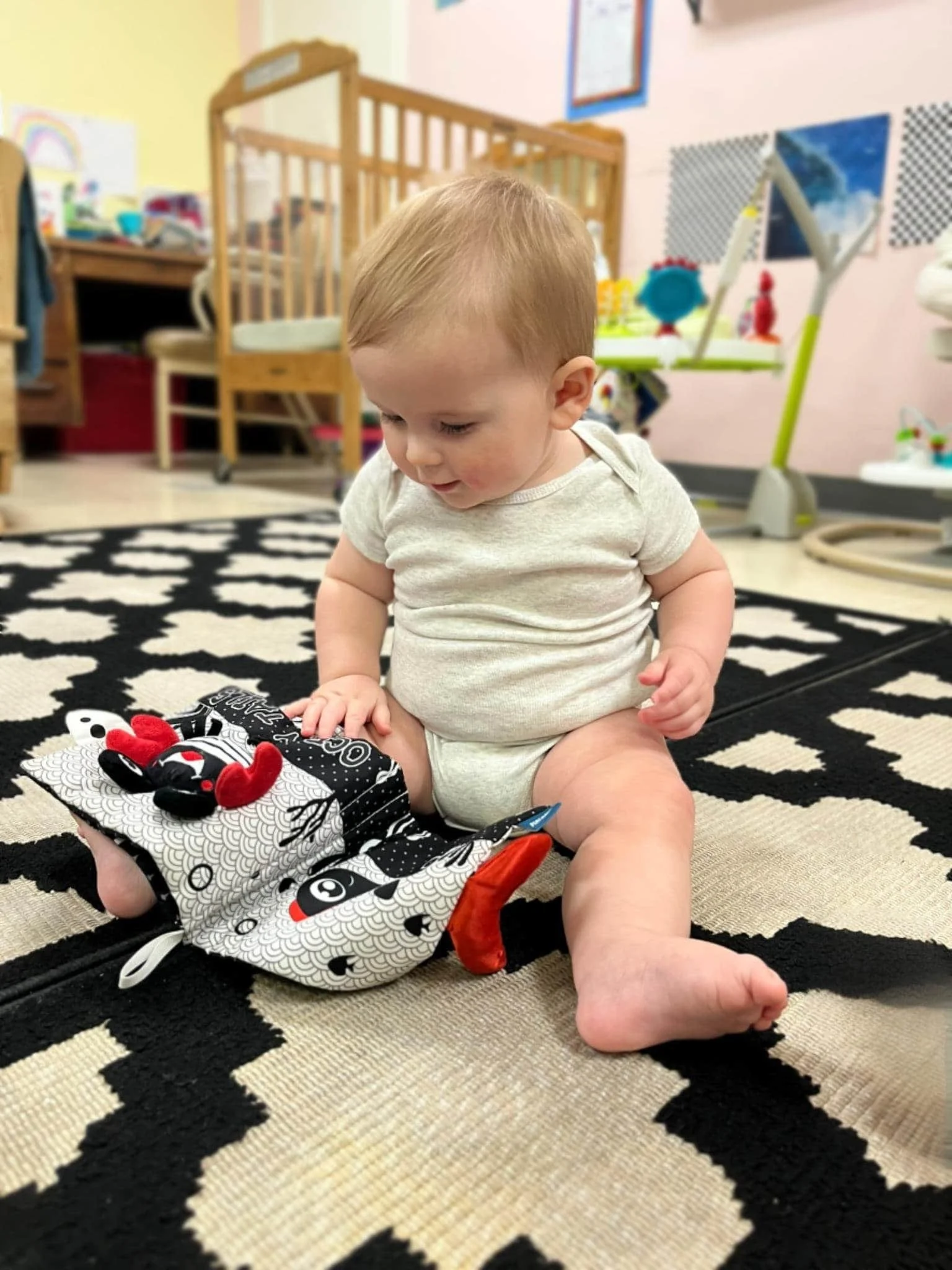 Infant sitting on rug, exploring a soft black-and-white Montessori cloth book at Town & Country Austin, Texas