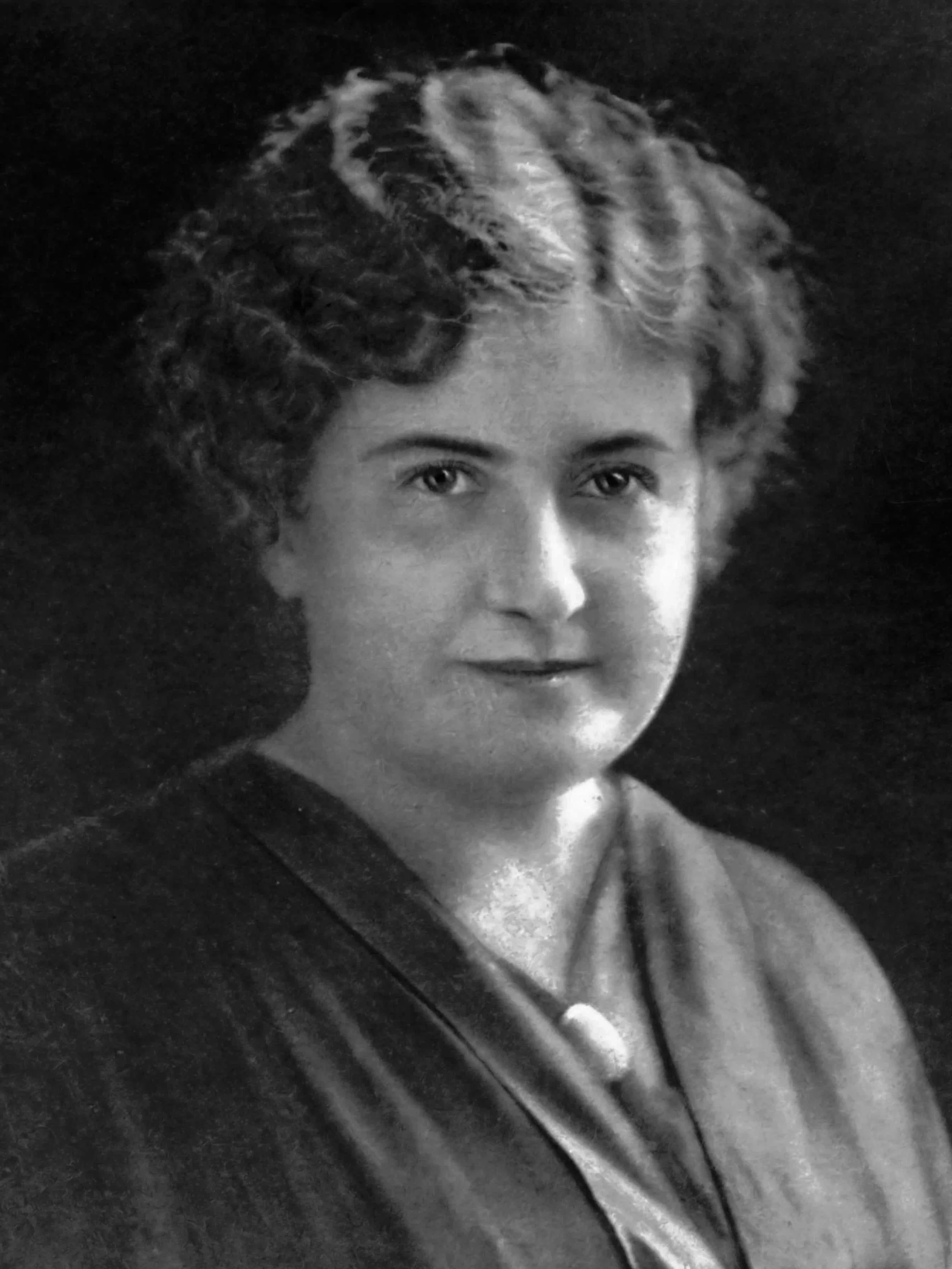 Black and white portrait of a woman with short, curly hair, wearing a dark top with a necklace.
