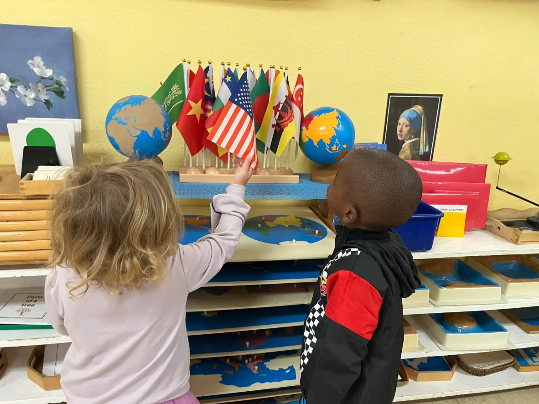 Children in a Montessori kindergarten in Austin working with world flags and maps, developing cultural awareness and hands-on geography skills.