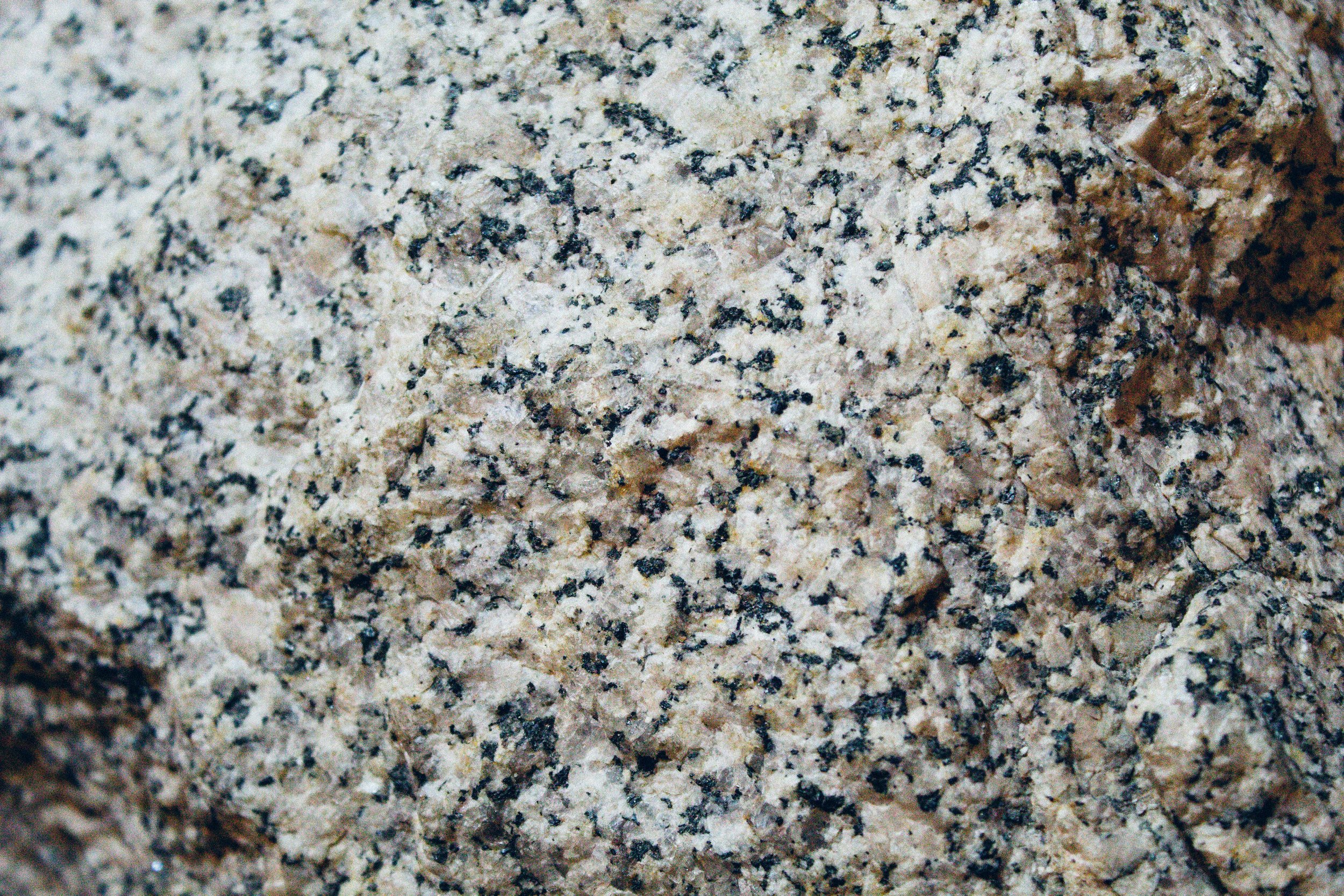 Close-up of granite surface with a coarse, speckled texture in tan and beige, flecked throughout with dark gray and black mineral grains.