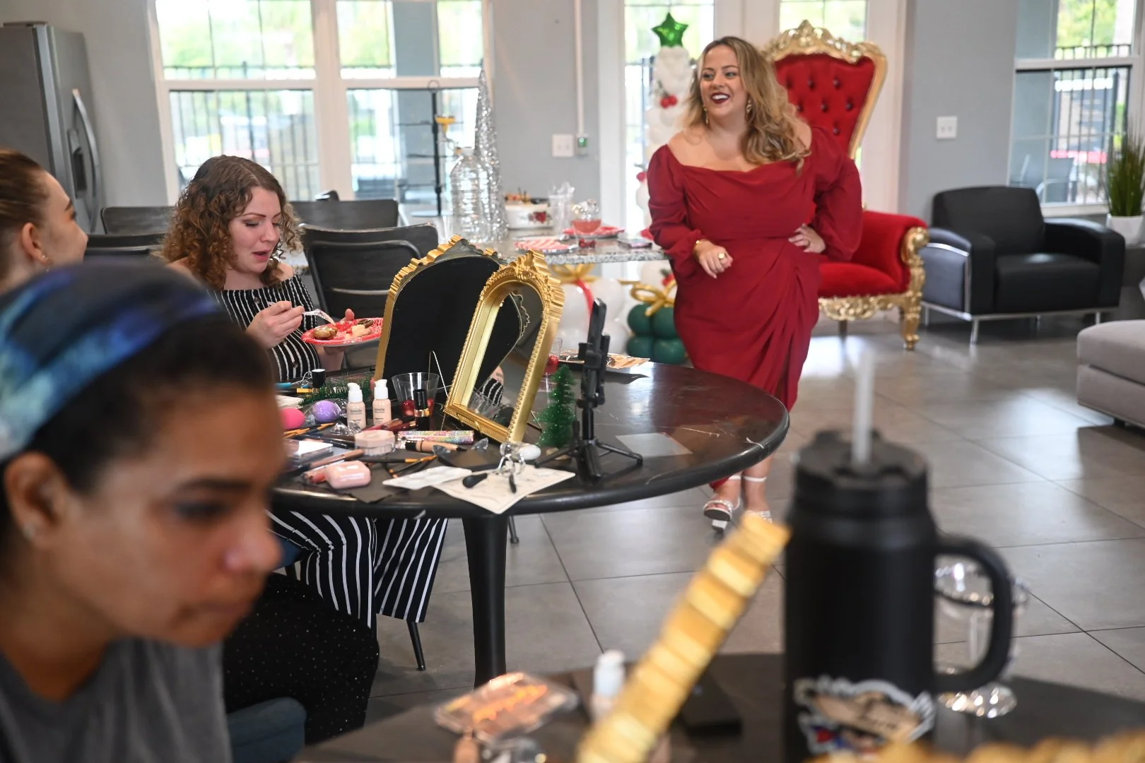 Women preparing for a Christmas-themed event with makeup and decorations in a cozy living room.