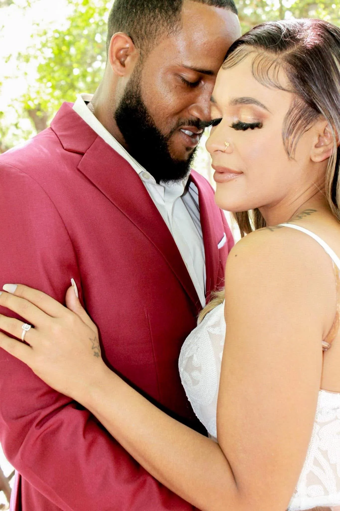 A man and woman sharing an intimate moment outside, with their foreheads touching and eyes closed.