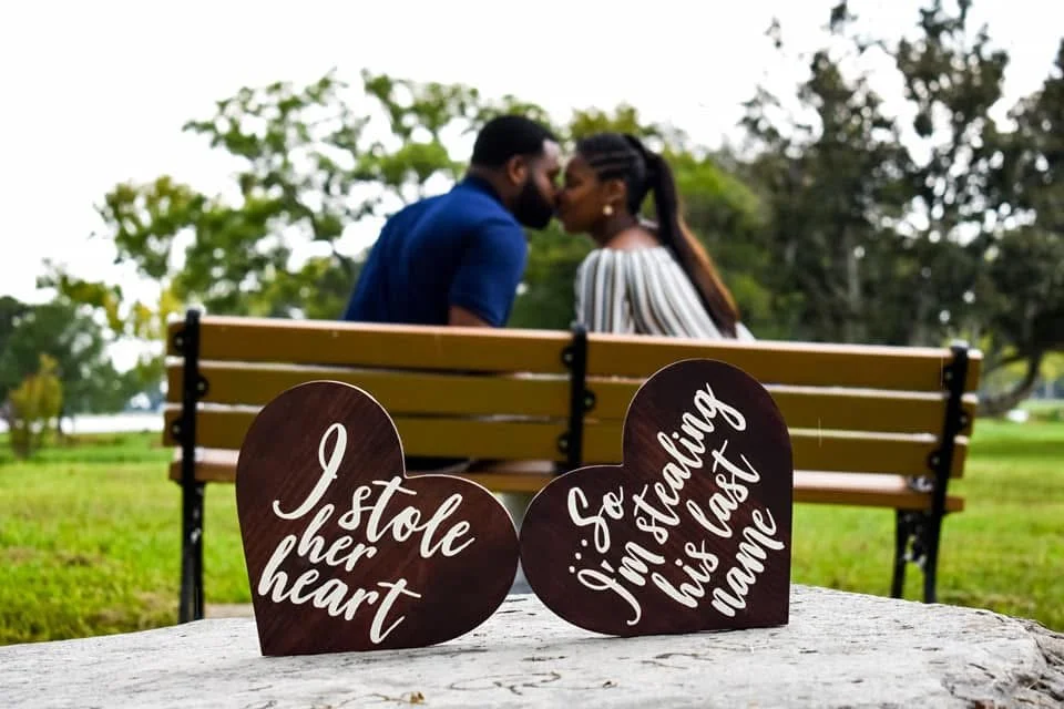 A couple sharing a kiss on a park bench with romantic heart-shaped signs in the foreground.