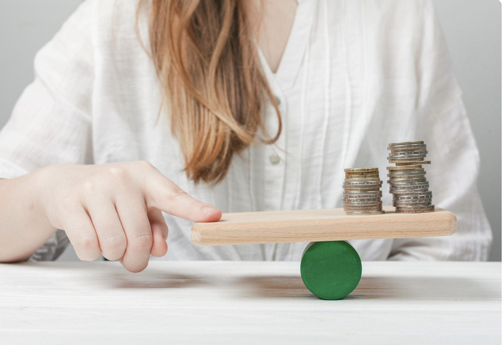 Person stacking coins on a balance scale with green and wooden elements.