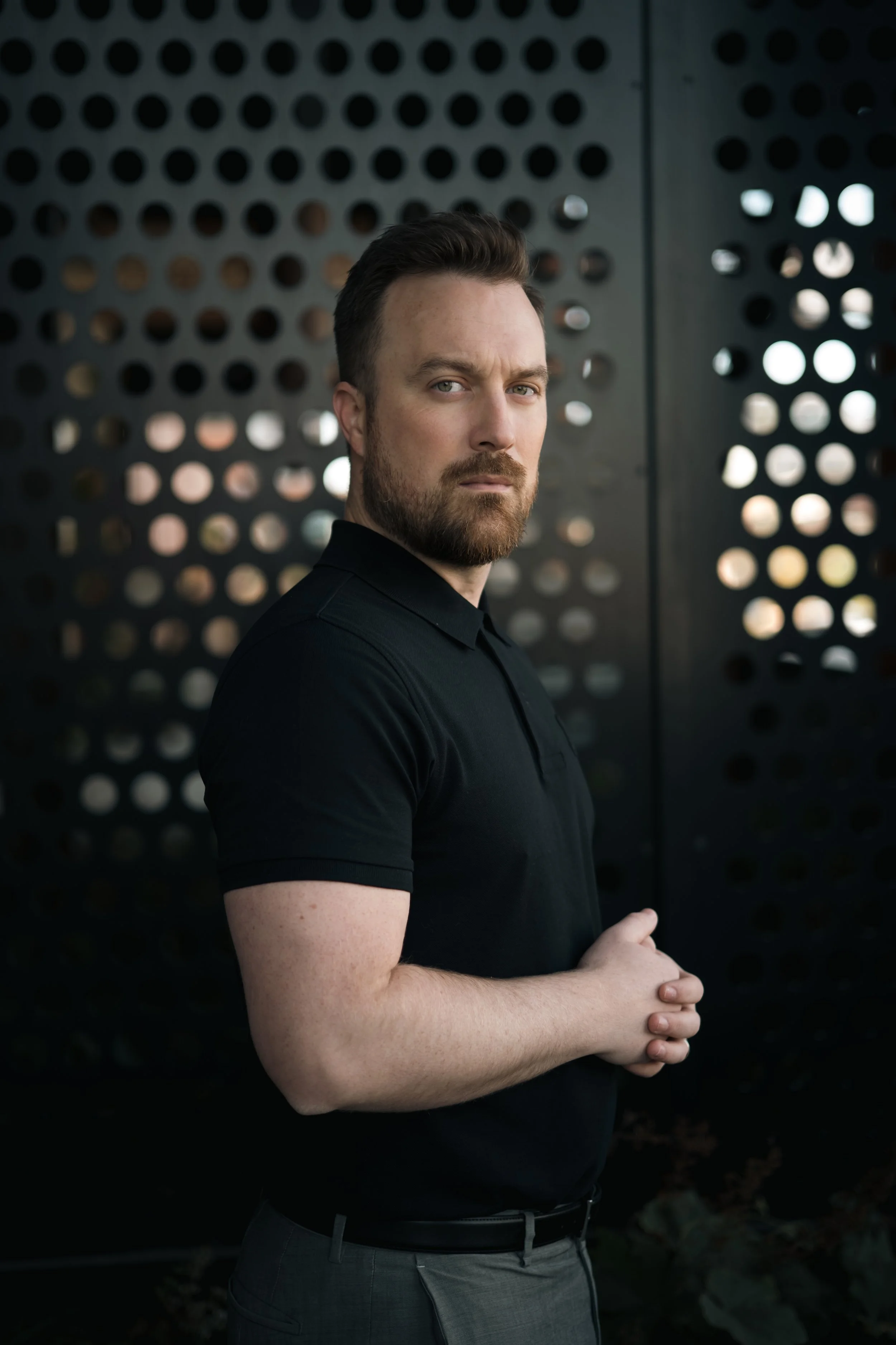 A smiling man with sunglasses and a striped shirt at a marina during sunset with yachts in the background.
