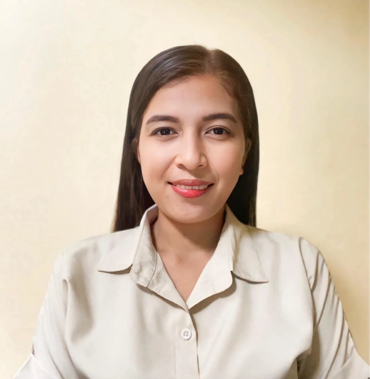 A woman with long dark hair wearing a beige button-up shirt, smiling against a plain light-colored background.