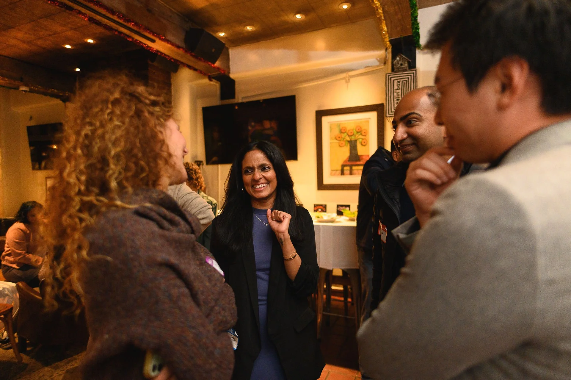 Group of diverse people smiling and engaging in conversation at an indoor gathering or party.