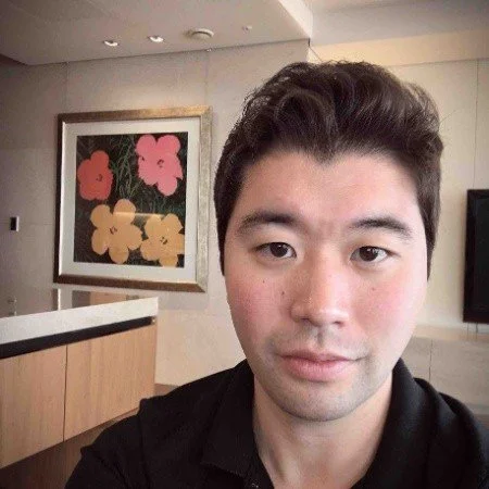 A young man with short, dark hair taking a selfie indoors.