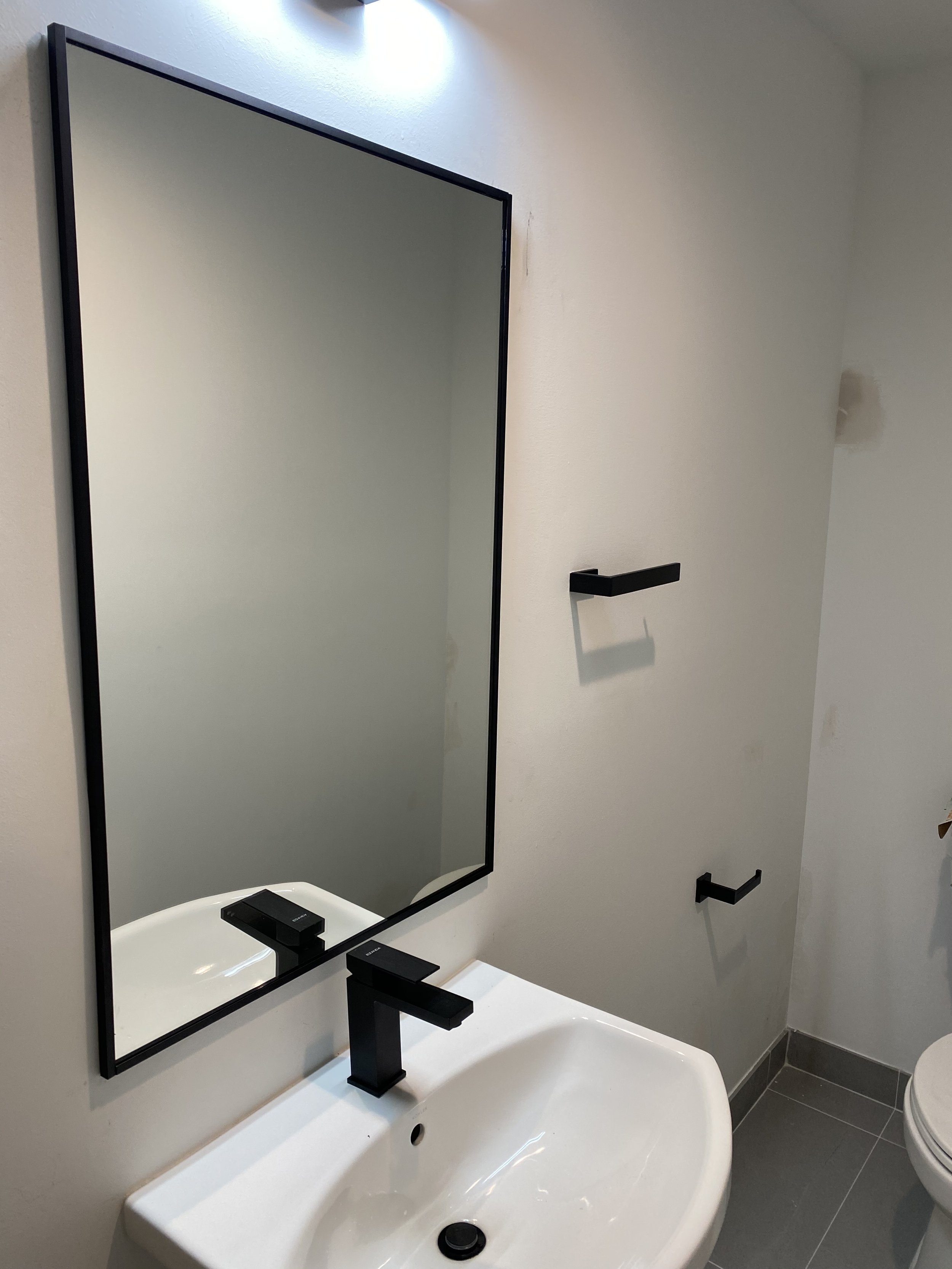Bathroom with a rectangular mirror, white sink with black faucet, black towel holders, and gray tiled floor.
