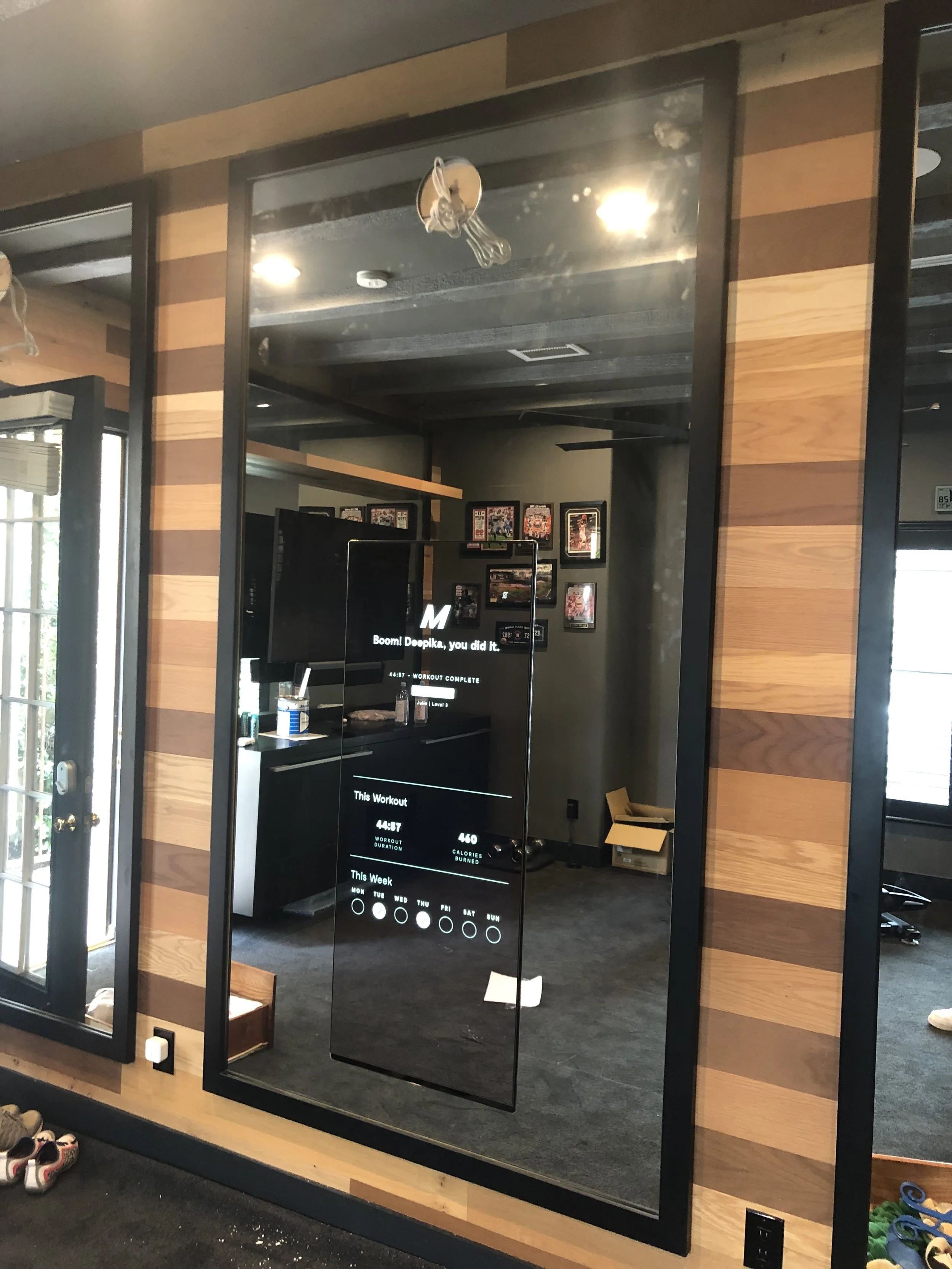Mirror in a gym showing a completed workout session with time and calorie details, reflecting a room with wooden wall panels, a TV, framed pictures, and gym equipment.