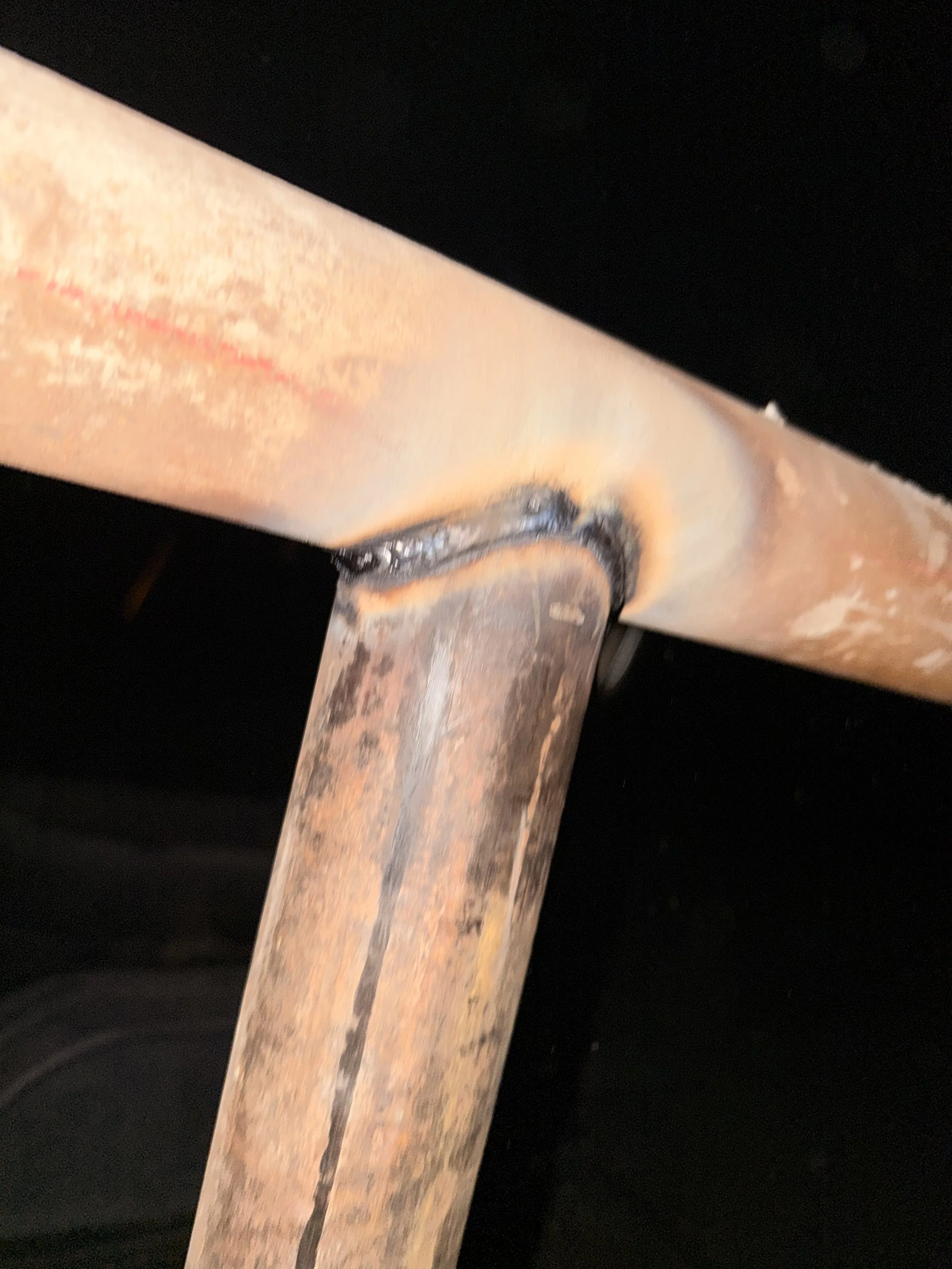 Close-up of a rusty metal pipe with a welded joint against a black background.