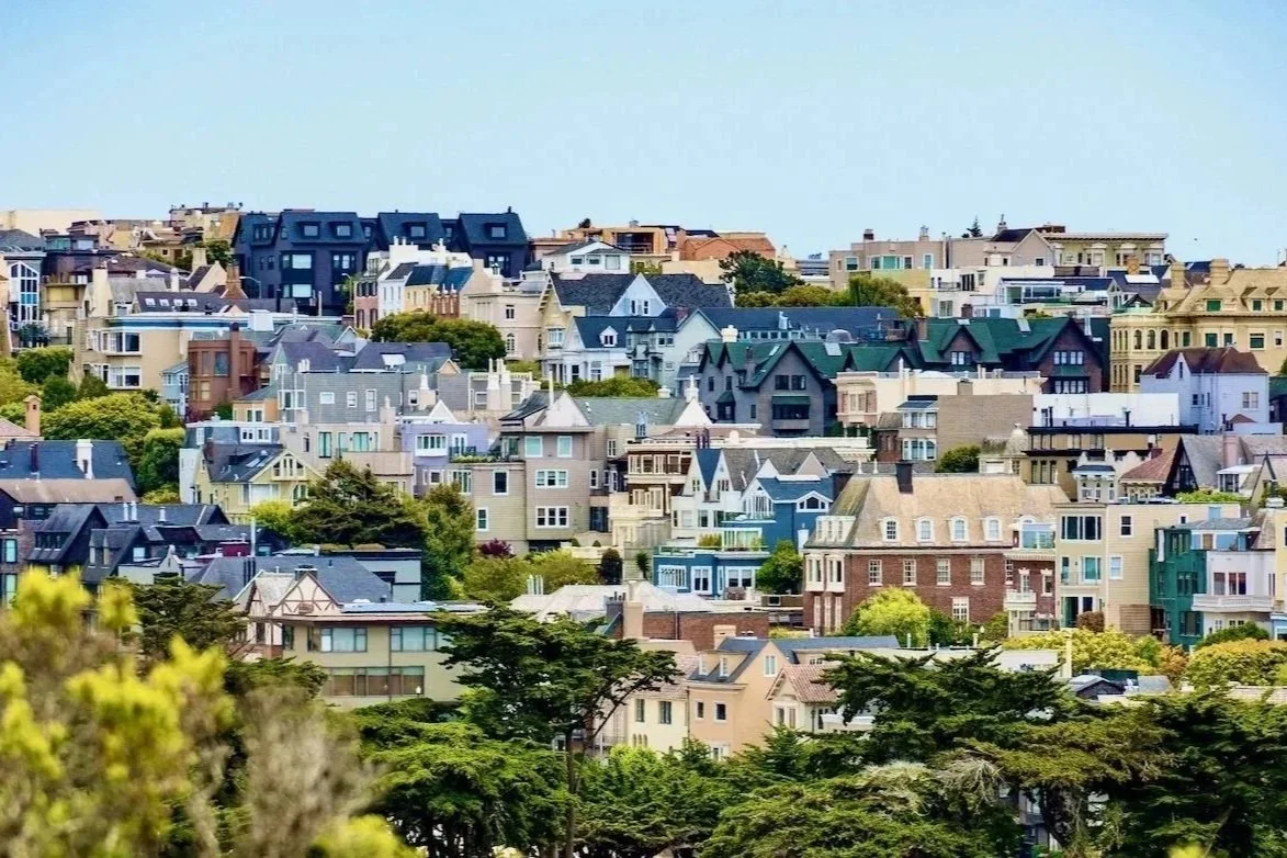 A hillside filled with multicolored residential houses with trees in the foreground and a clear blue sky.