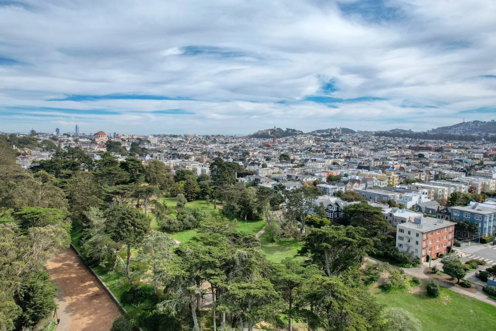 A panoramic view of a cityscape with rolling hills, tall buildings, and a cloudy sky above.