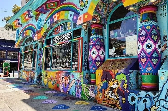 Colorful mural-painted building with rainbow, hearts, faces, and characters, featuring large blue and purple decorative columns.