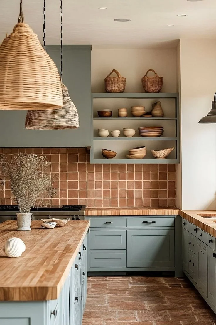 The image shows a kitchen with light blue cabinets, a wooden countertop, open shelves with bowls and baskets, beige tiles on the wall, and hanging wicker lamps.