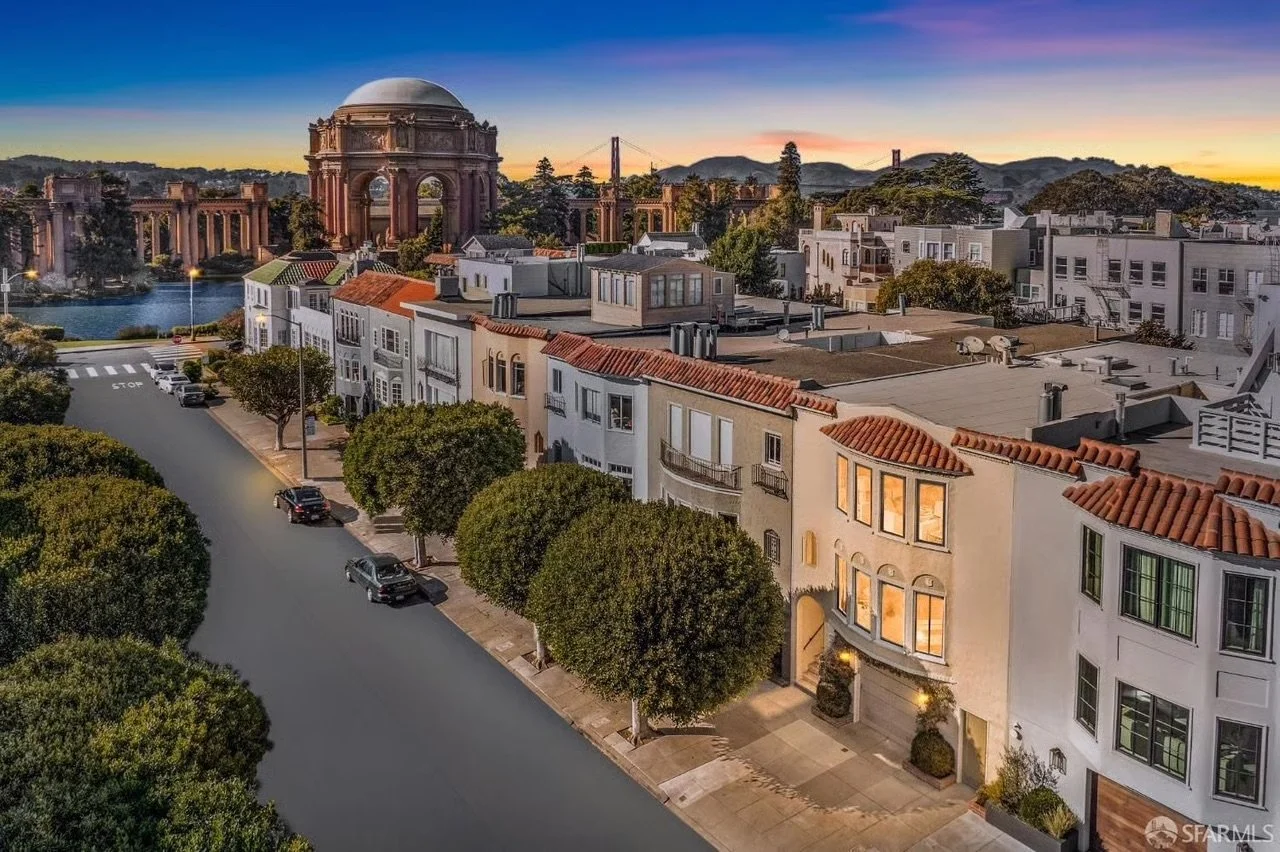 Aerial view of San Francisco neighborhood at sunset with trees, residential buildings, and the Palace of Fine Arts in the background.