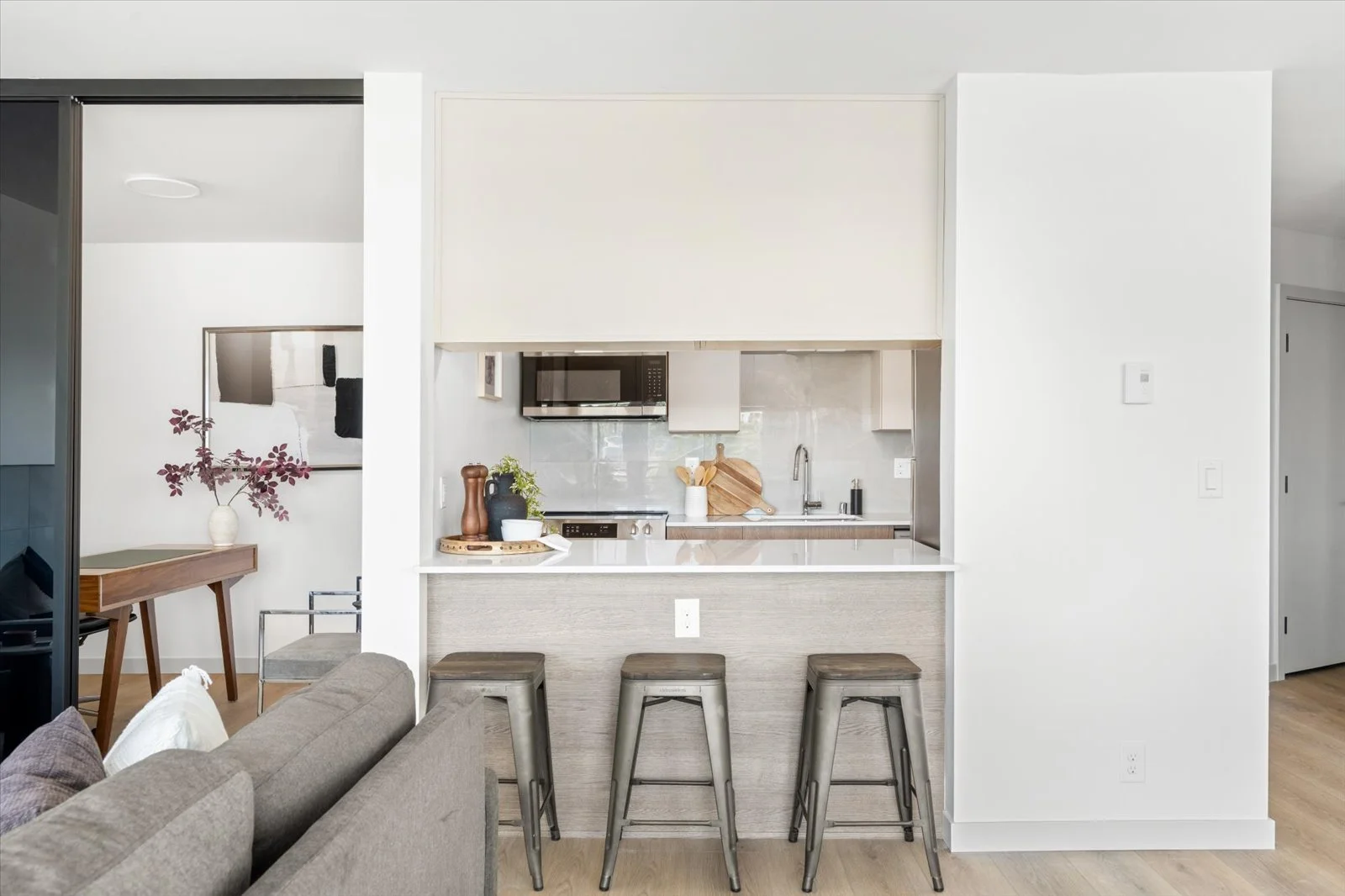 Modern kitchen with white cabinets, gray countertops, and three metal bar stools at the breakfast bar