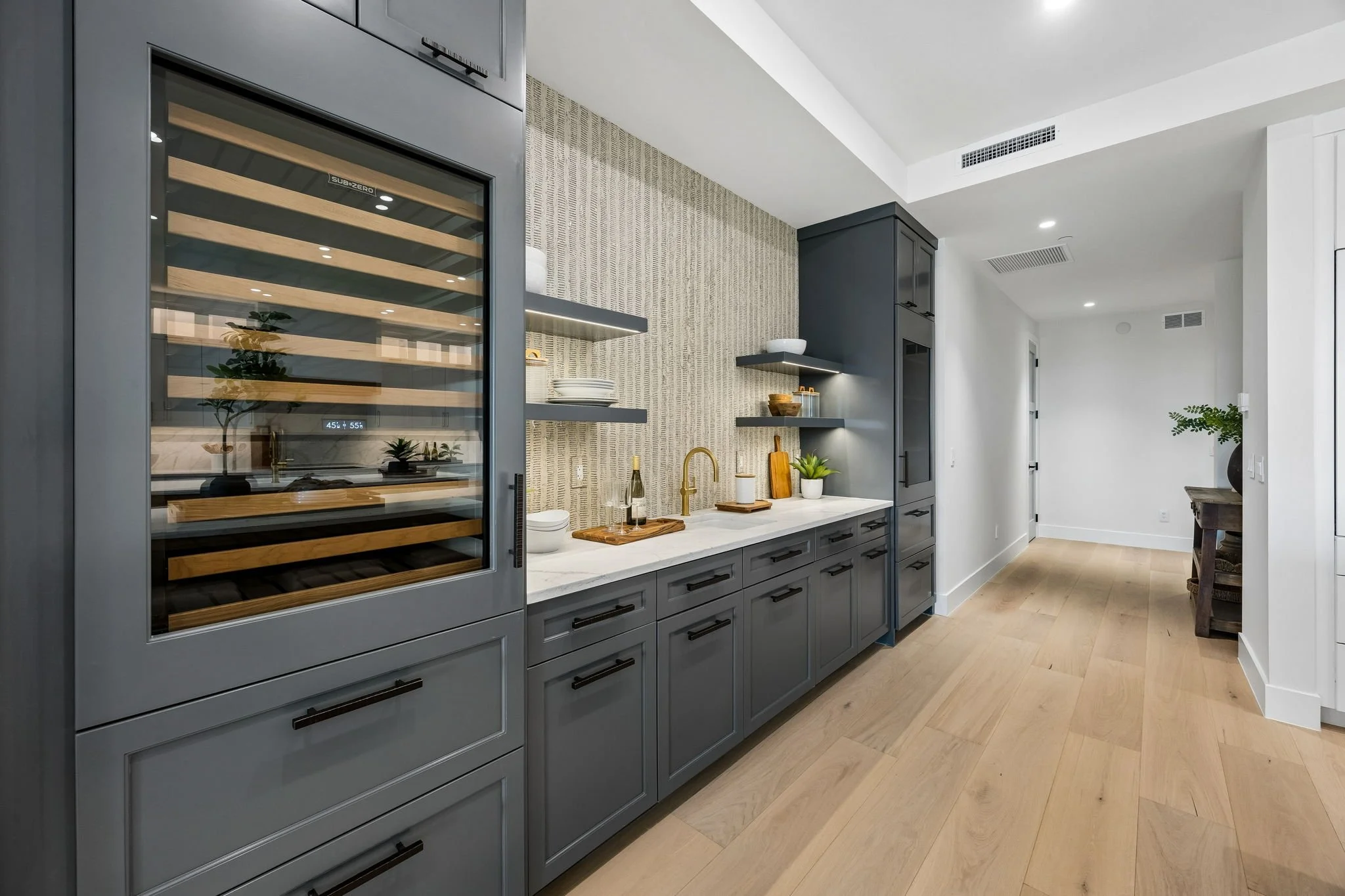 Modern kitchen with gray cabinets, open shelves, a built-in wine cooler, and light wood flooring.