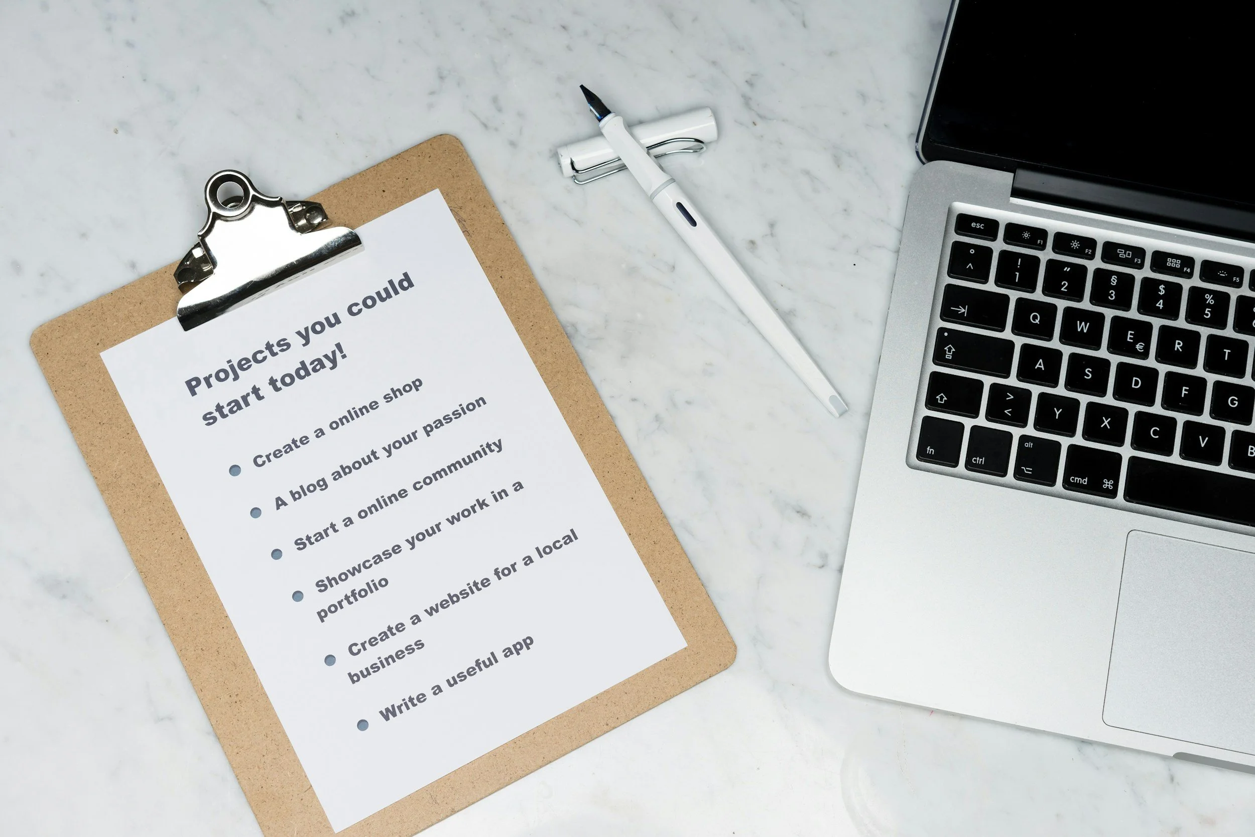 A clipboard with a list titled 'Projects you could start today!' next to a laptop, pen, and marble surface.