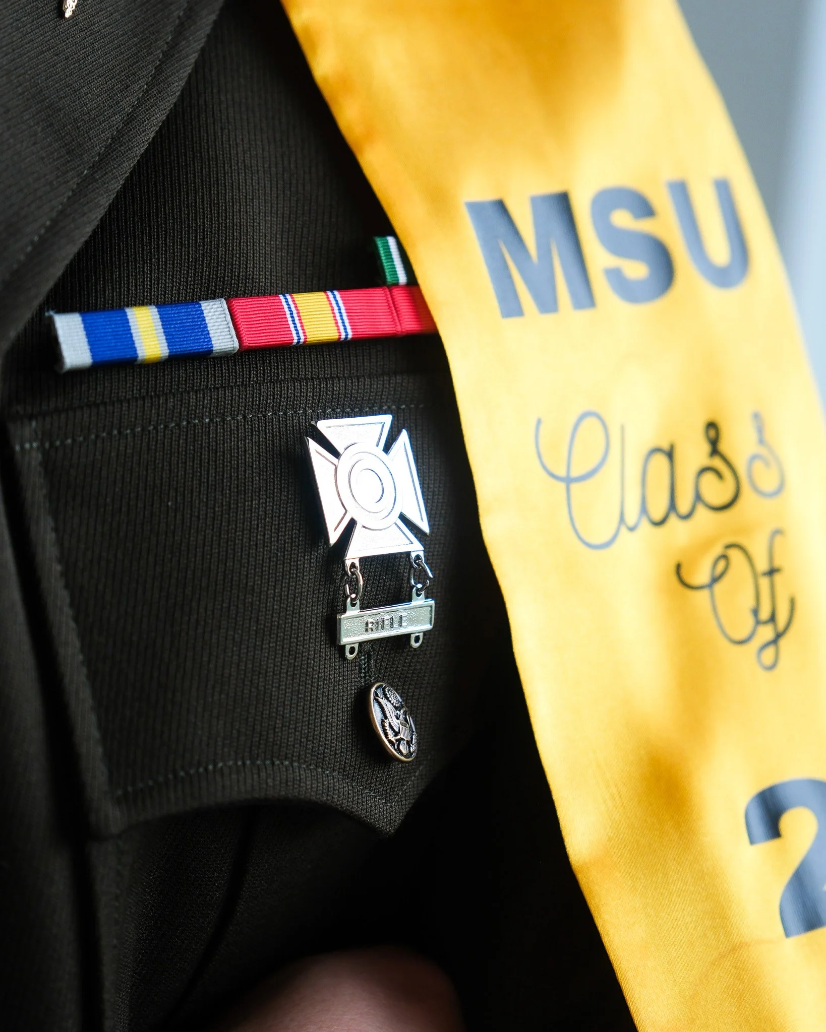Close-up of a black backpack with a graduation medal, a colorful striped ribbon, and a yellow sash displaying 'MSU Class of 2023'.