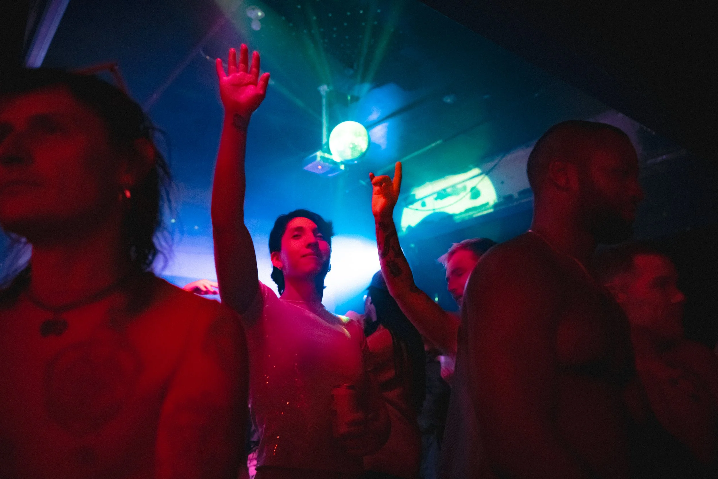 People dancing at a nightclub with colorful lights and a full moon projection on the ceiling.