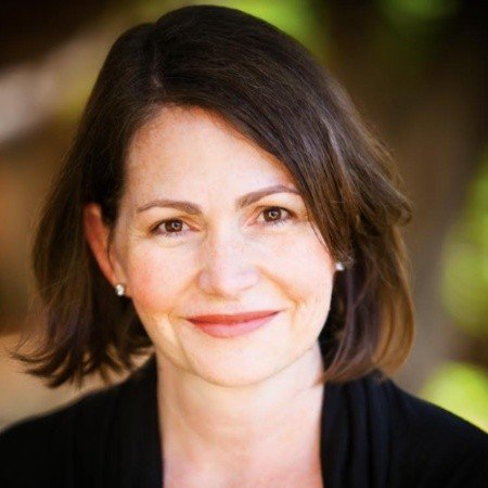 Close-up of a woman with shoulder-length brown hair smiling outdoors.