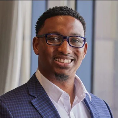 Portrait of a man with glasses in a business suit smiling indoors.