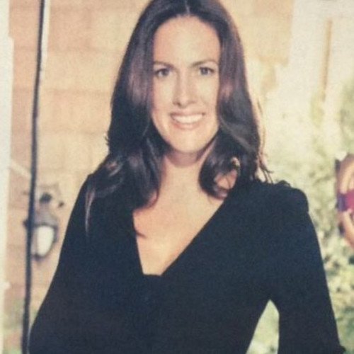 A woman with long brown hair wearing a black top, smiling outdoors.