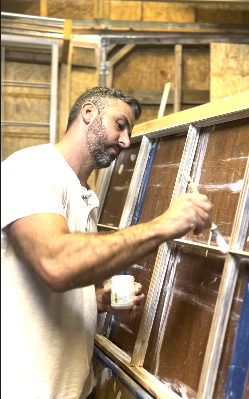 A man painting a wooden frame inside a workshop.