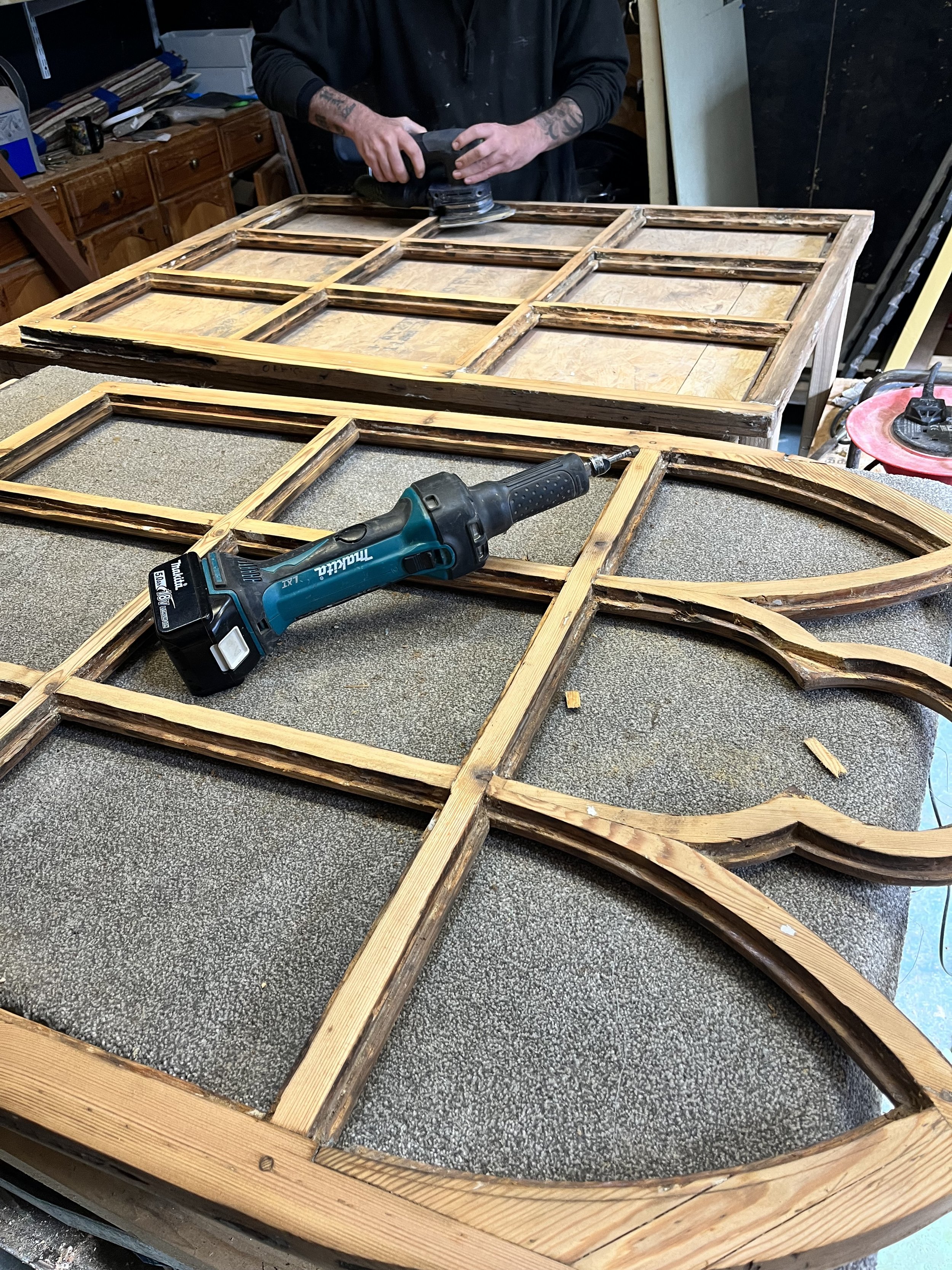 Person working on a wooden window frame with power tools in a workshop.