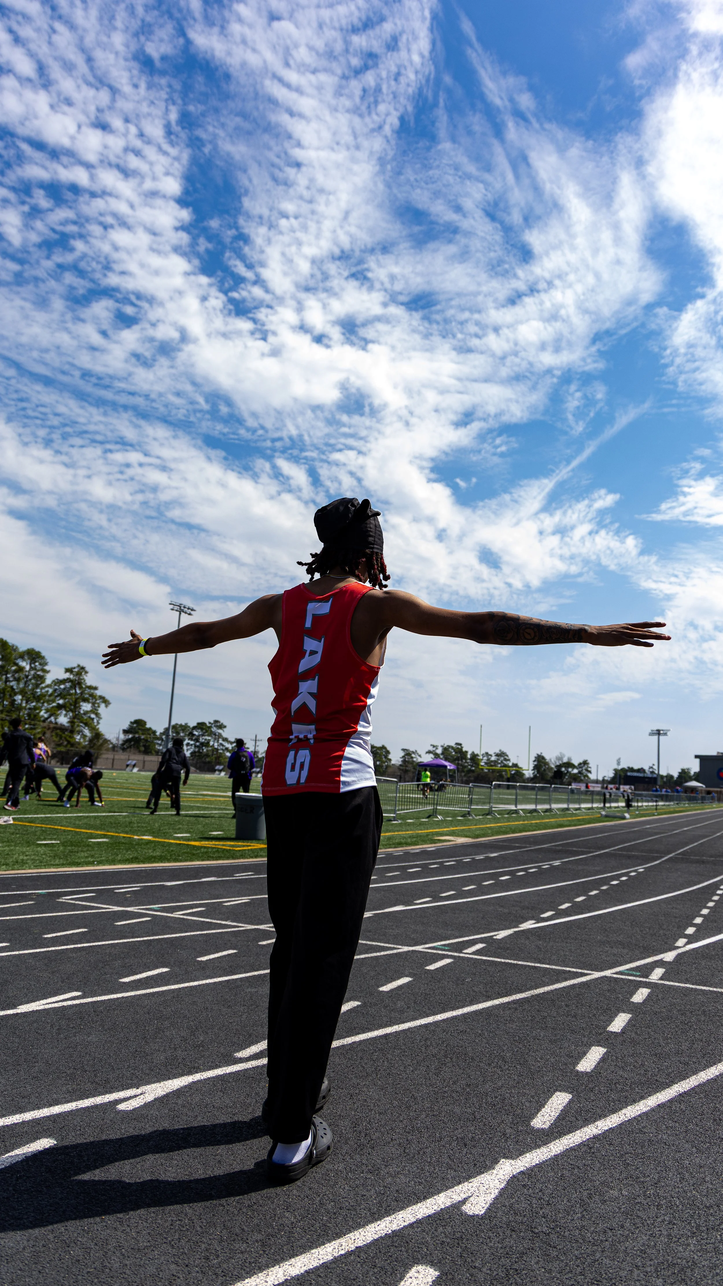 Track athlete warming up on a running track under a partly cloudy sky at a sports field.
