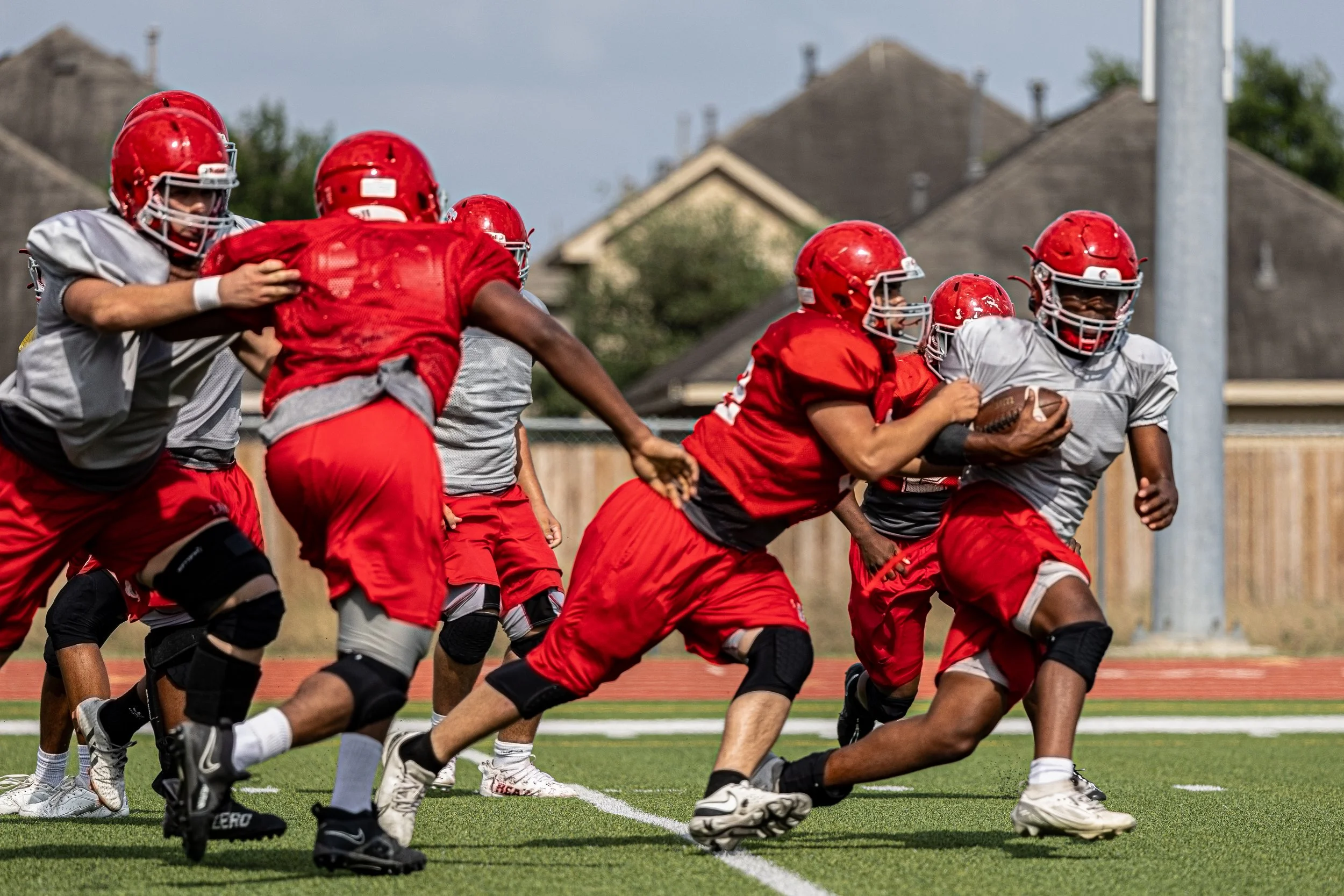 A group of football players practicing on the field, with one player running while holding the football as others block or chase him.