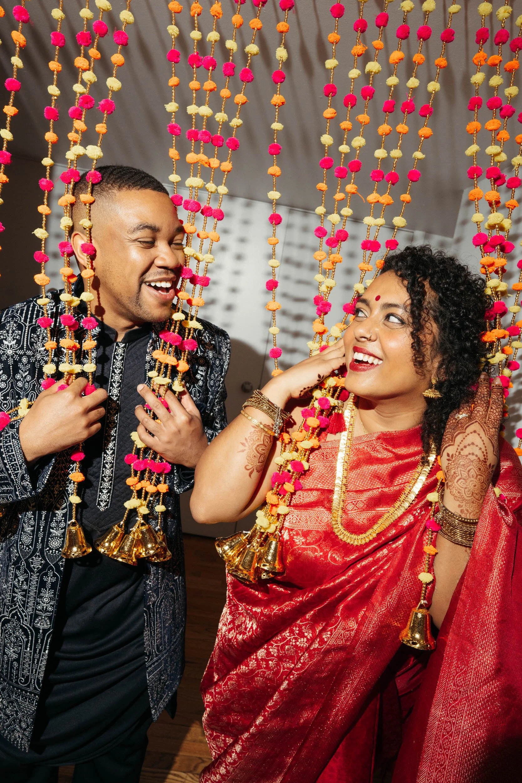 A couple smiling while standing in between colorful beads hanging from above