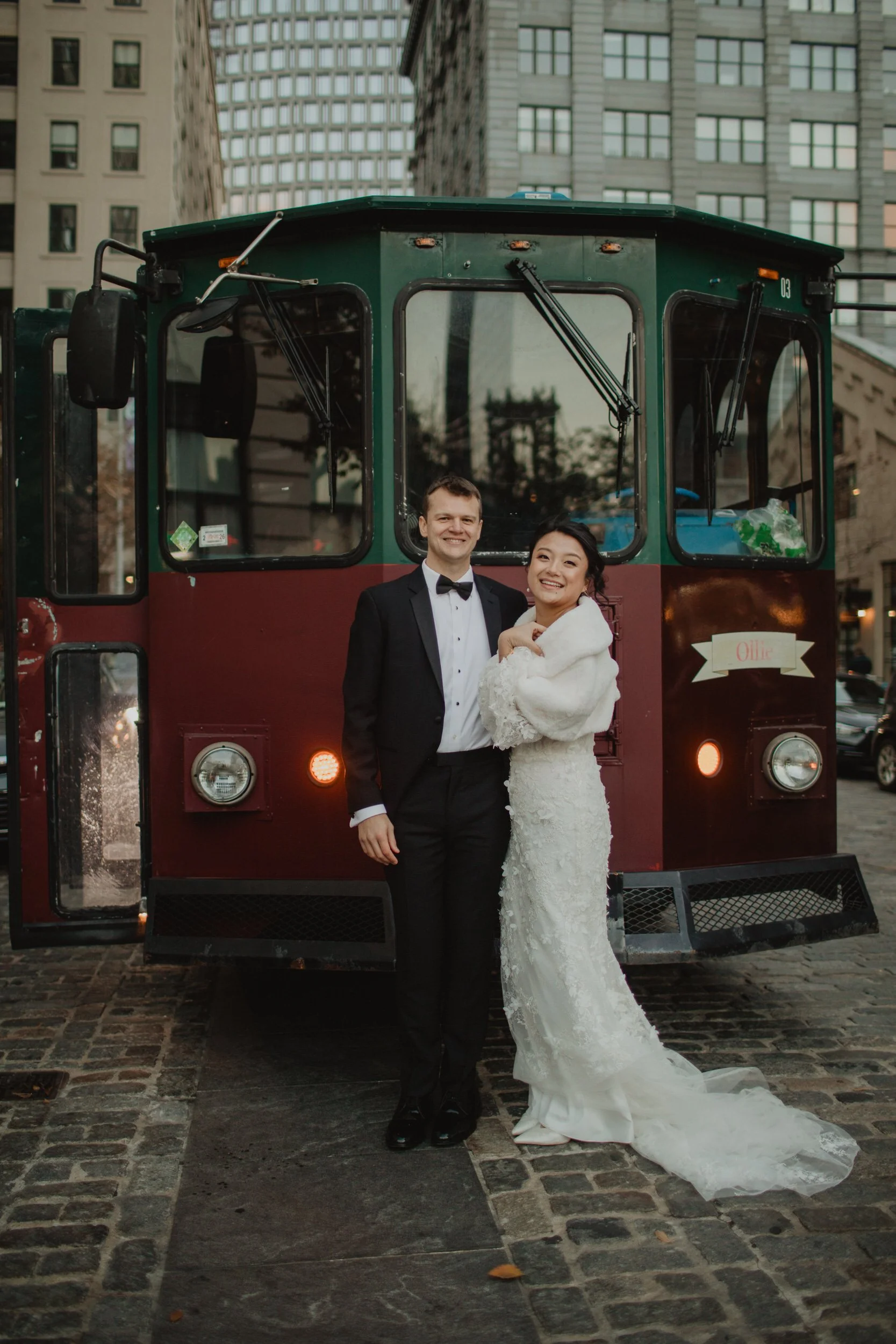 a newlywed couple smiling together and standing in front of a trolley