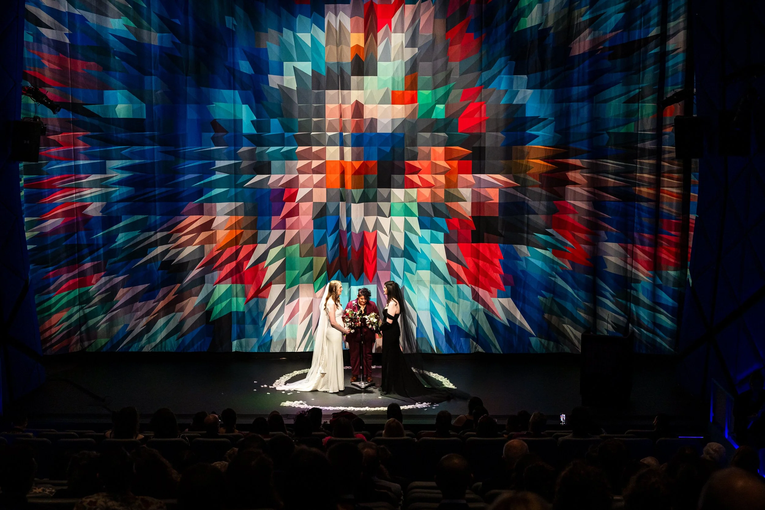 A couple standing on a stage with a colorful curtain behind them as they say their vows during their wedding ceremony