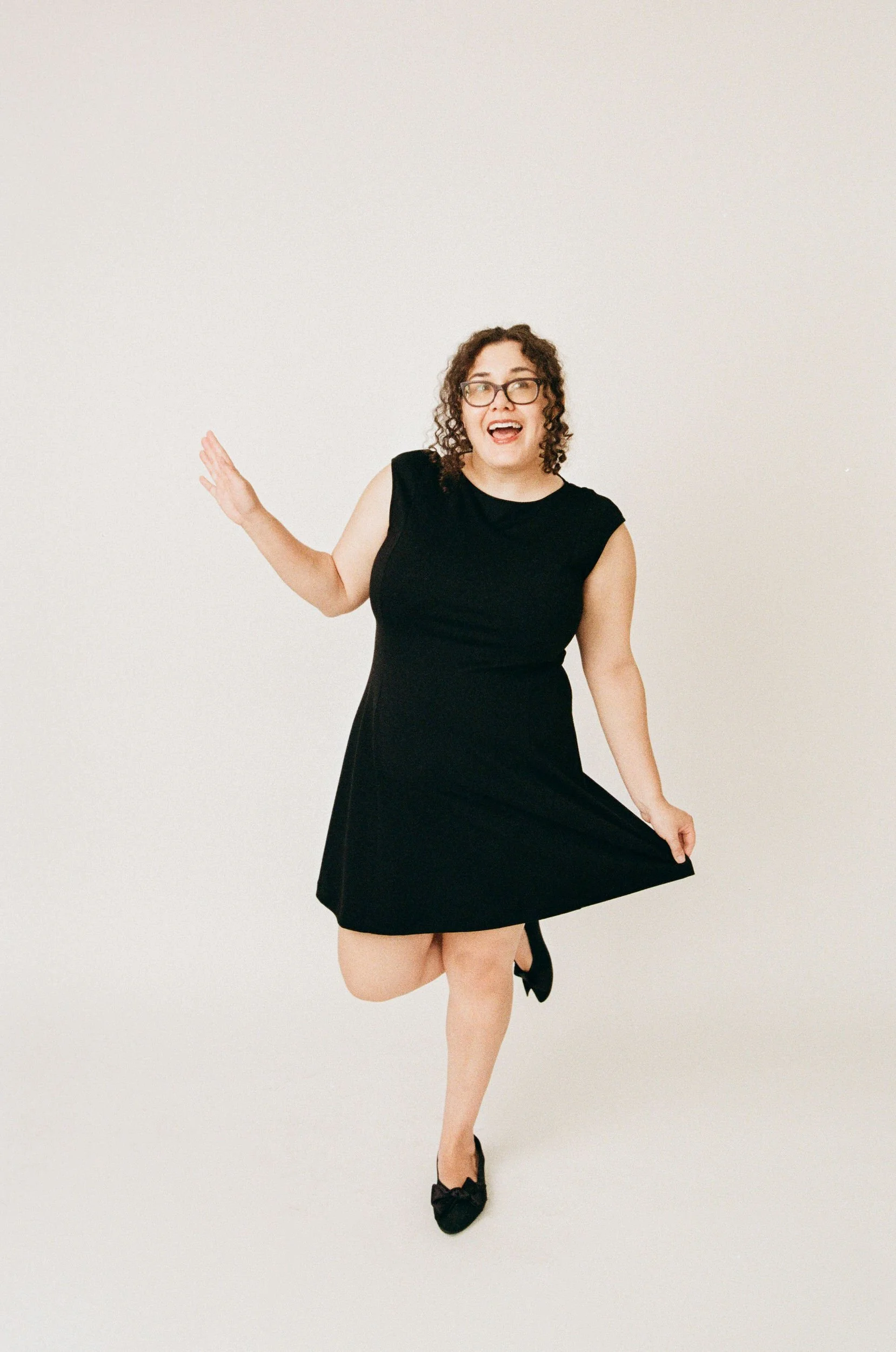 Marissa with one foot kicked up behind her as she holds the bottom of her dress with one hand