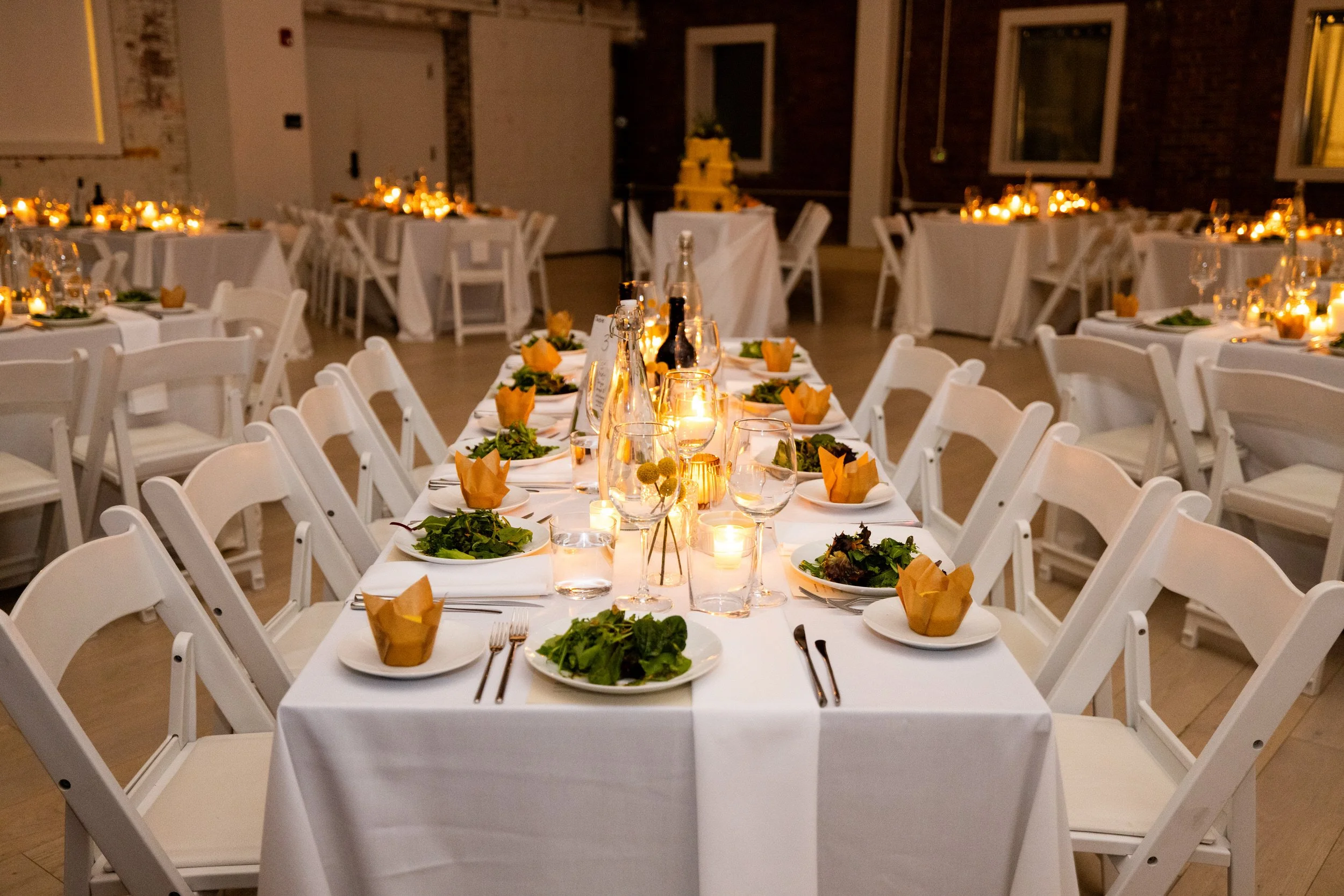 A wedding reception hall with rectangular table set with plates and small candles