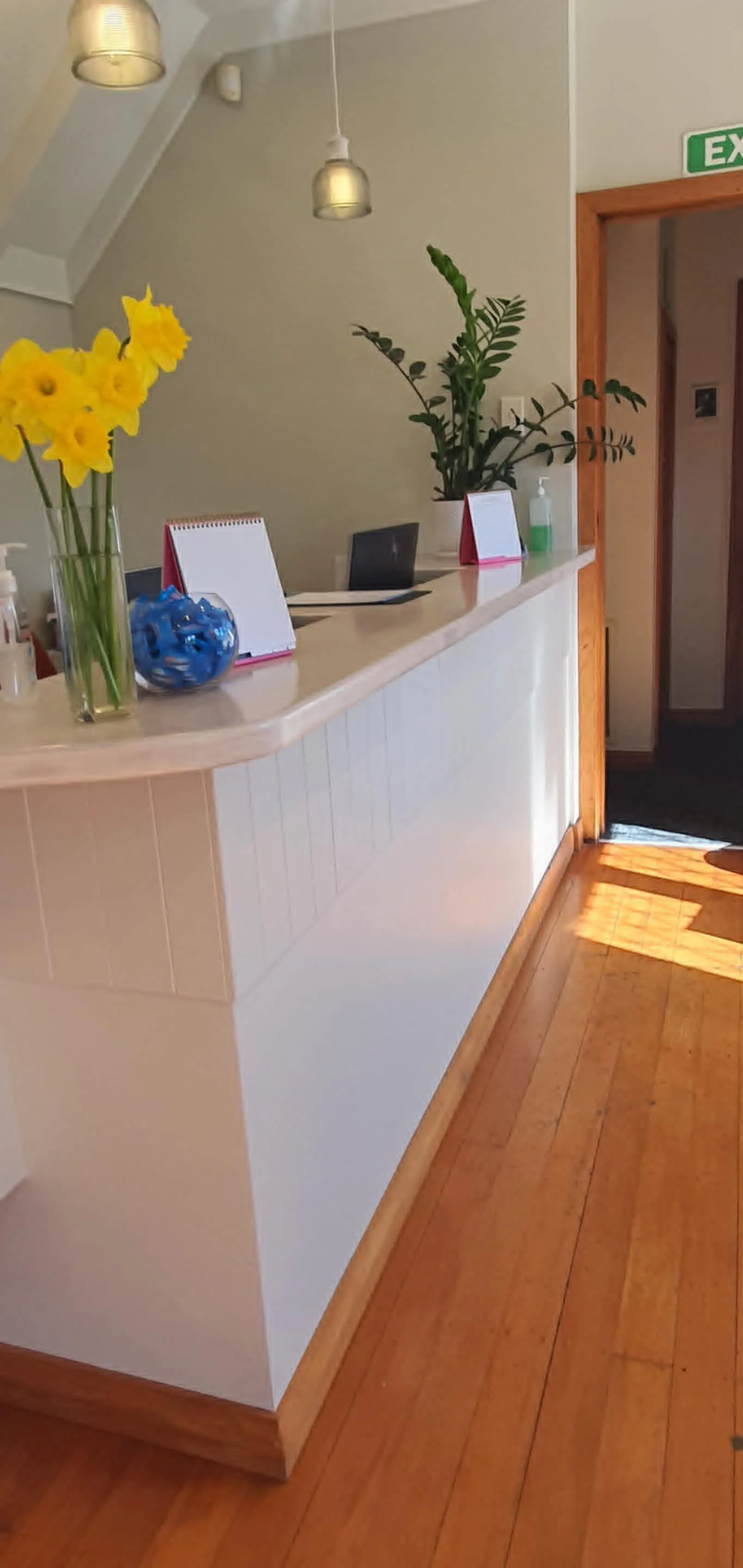 Reception desk with yellow flowers, decorative objects, and plants in an indoor area with wooden flooring and modern lighting.