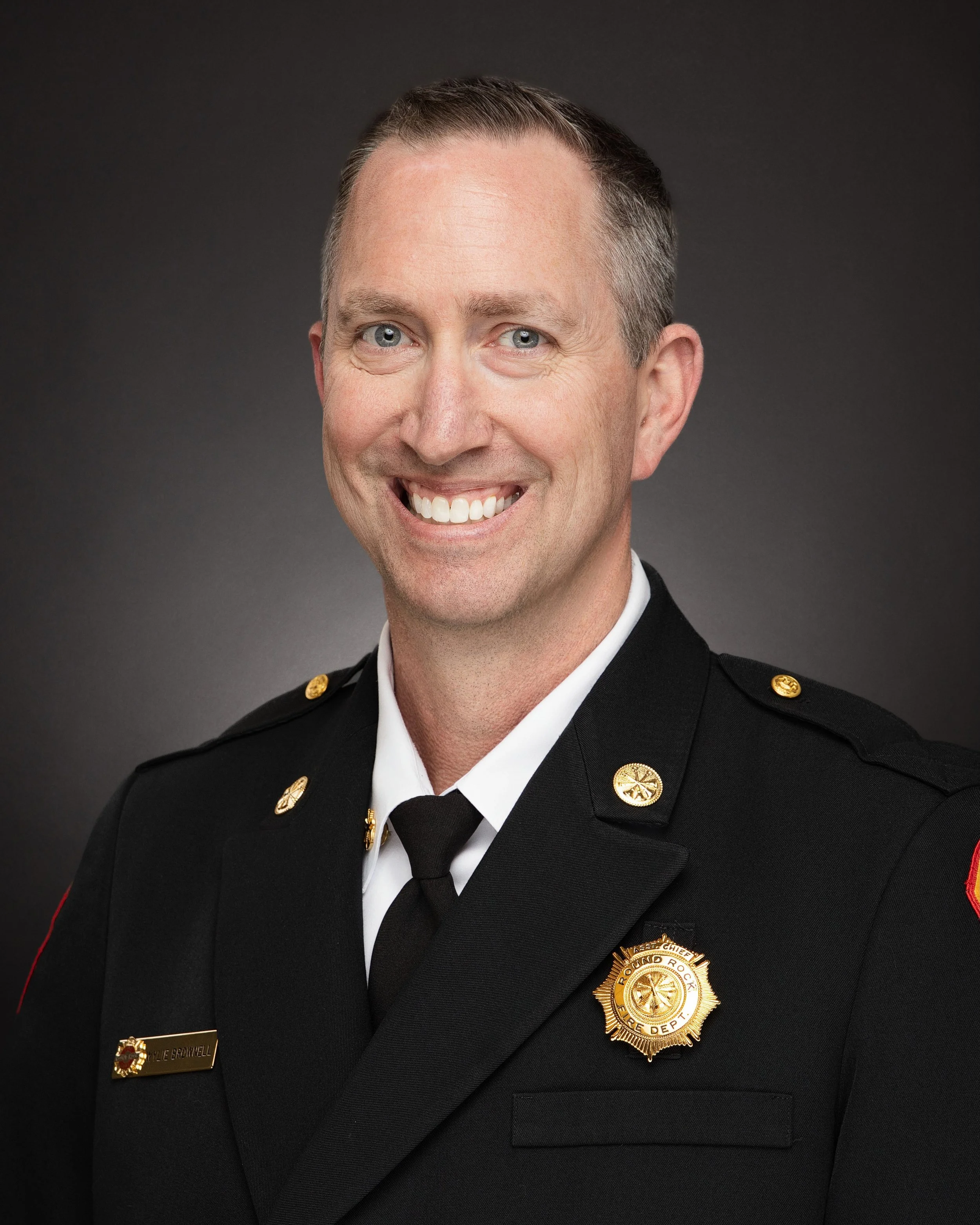 Portrait of a smiling male firefighter in uniform posing against a dark background.