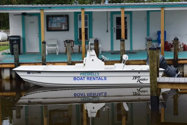 Boat docked at the marina with a building in the background, blue and yellow accents, and a sign that says 'Presnell's Boat Rentals'.