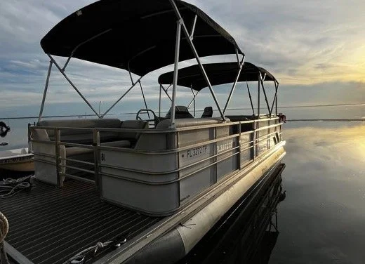 Pontoon boat on calm water during sunset.