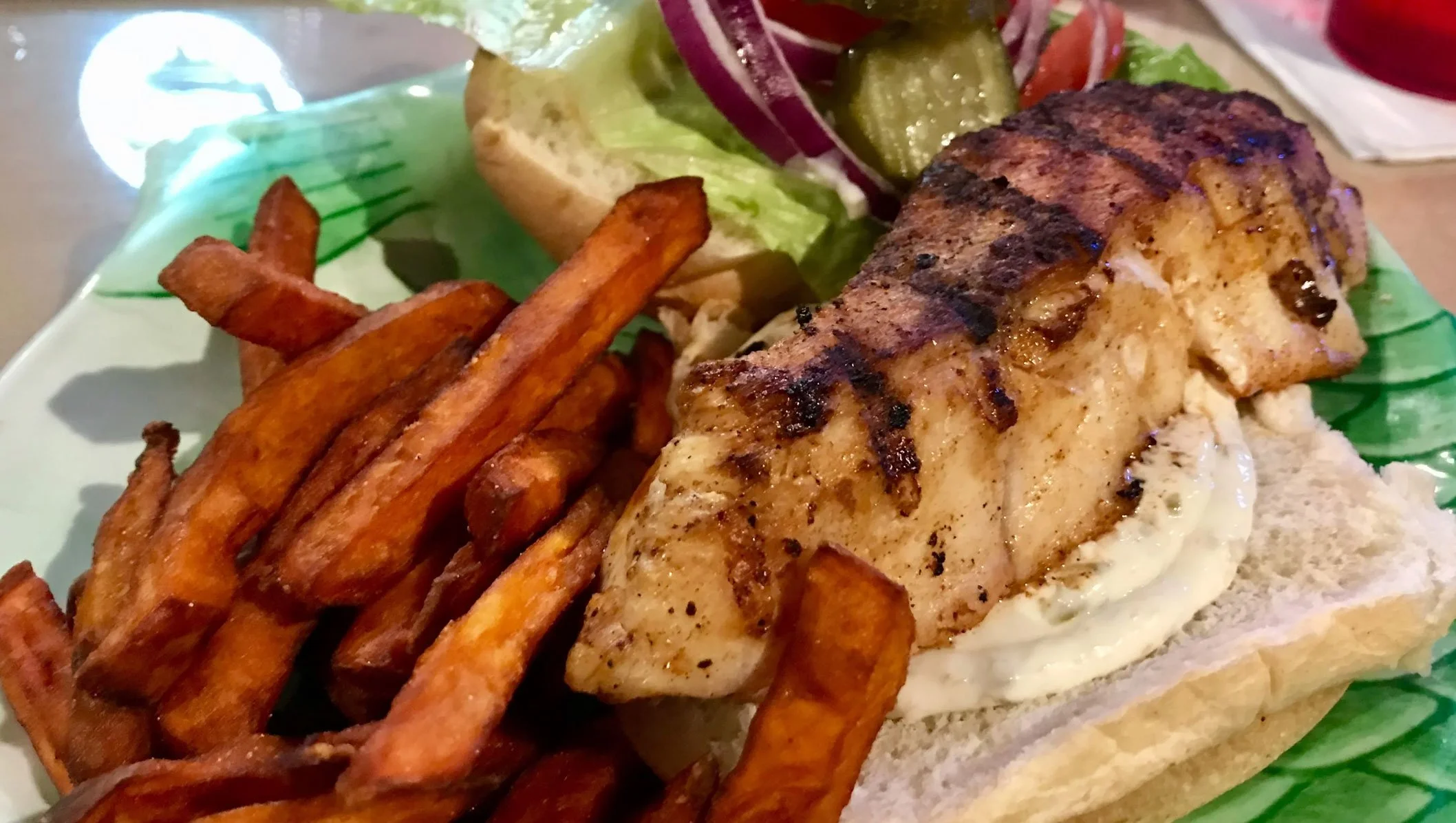 Grilled chicken sandwich with fries and a side salad on a green plate.