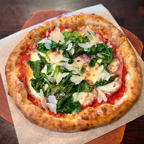 Fresh pizza topped with spinach, cheese, and shredded Parmesan cheese on a wooden table.