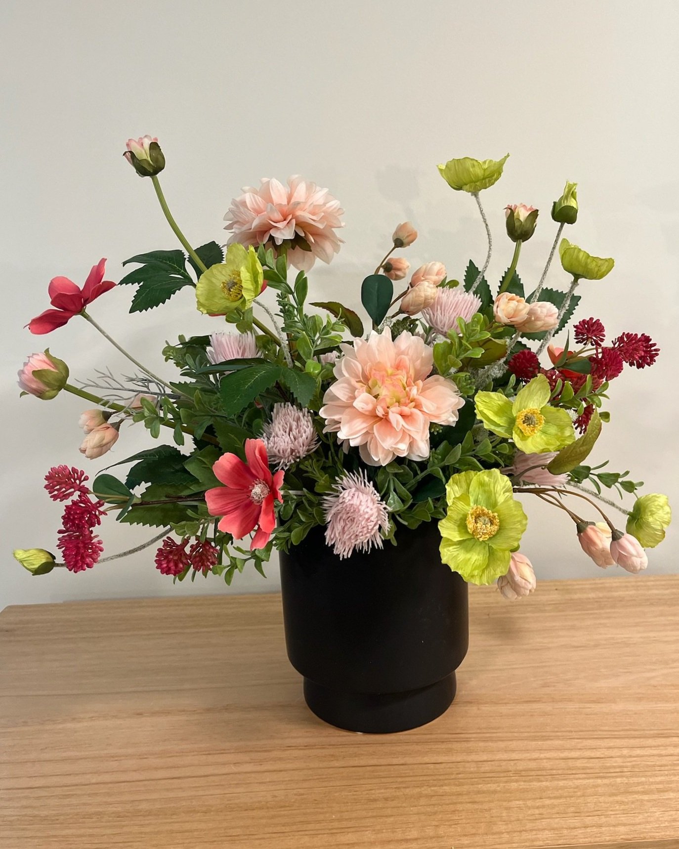 A colorful bouquet of various flowers in a black vase on a wooden surface.