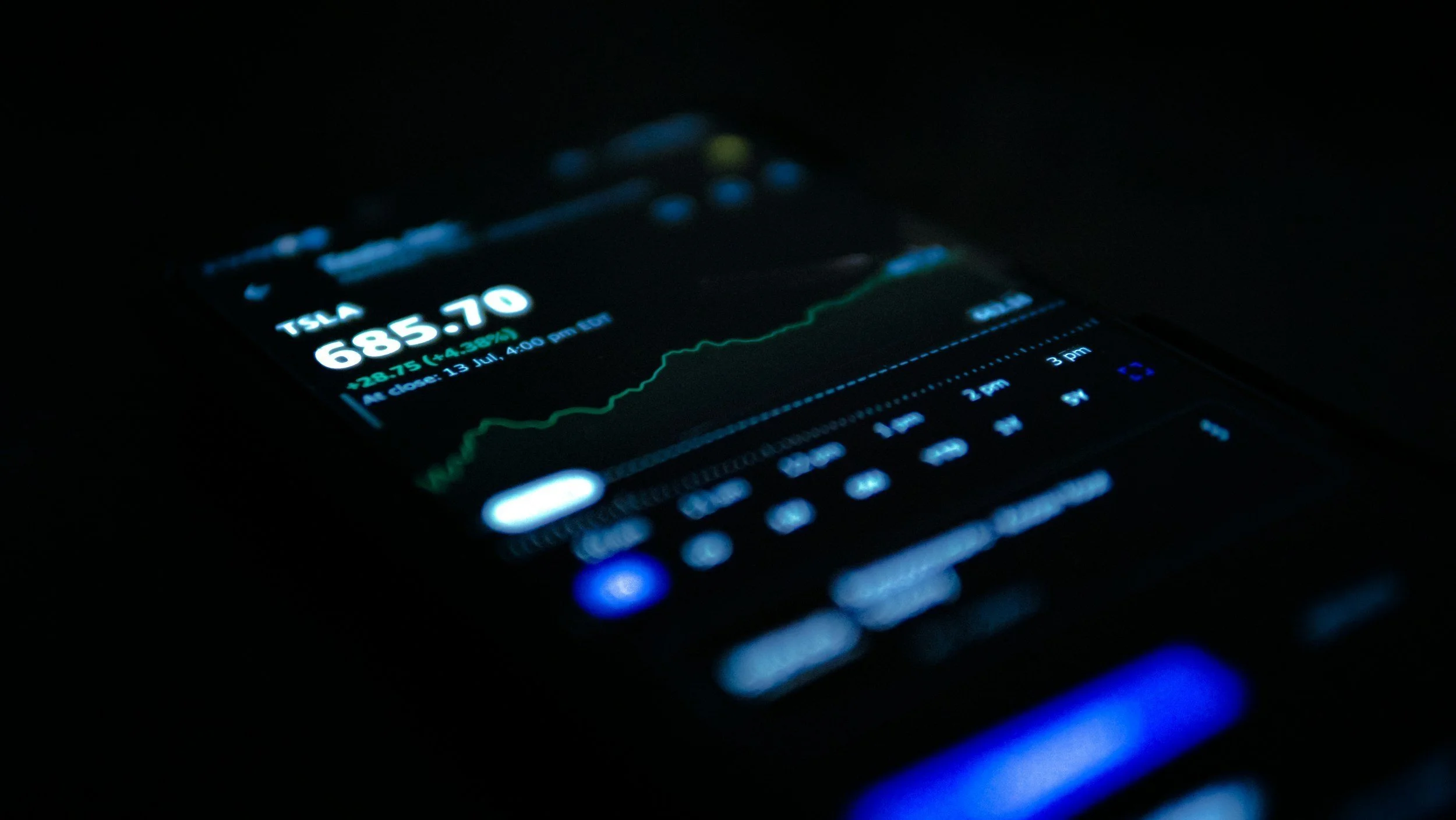 A smartphone screen displaying stock market information for Tesla with stock price, percentage change, and a graph in a dark environment.