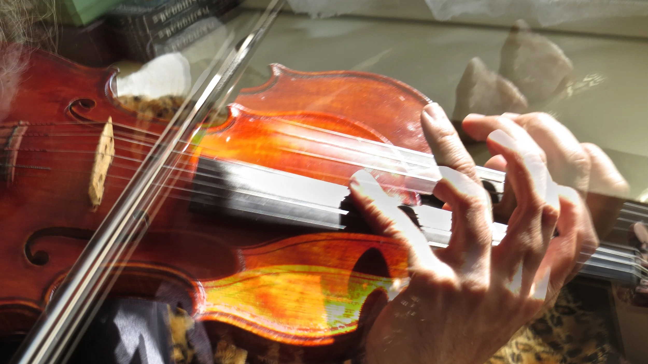Person playing a violin, captured through a glass reflection.